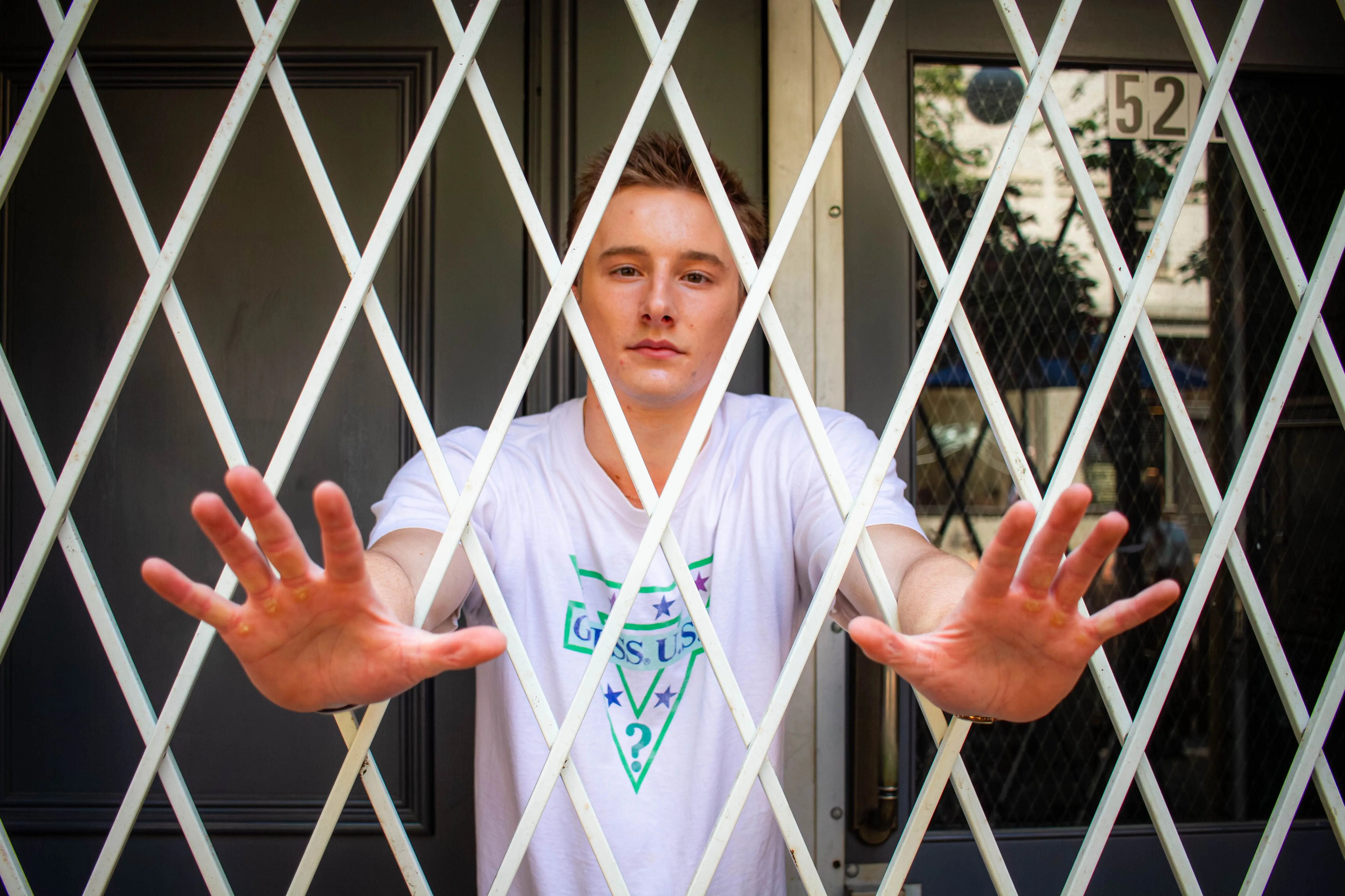 how to catch a rat Young man standing behind a metal gate with open hands, expressing emotions of entrapment in a city environment.