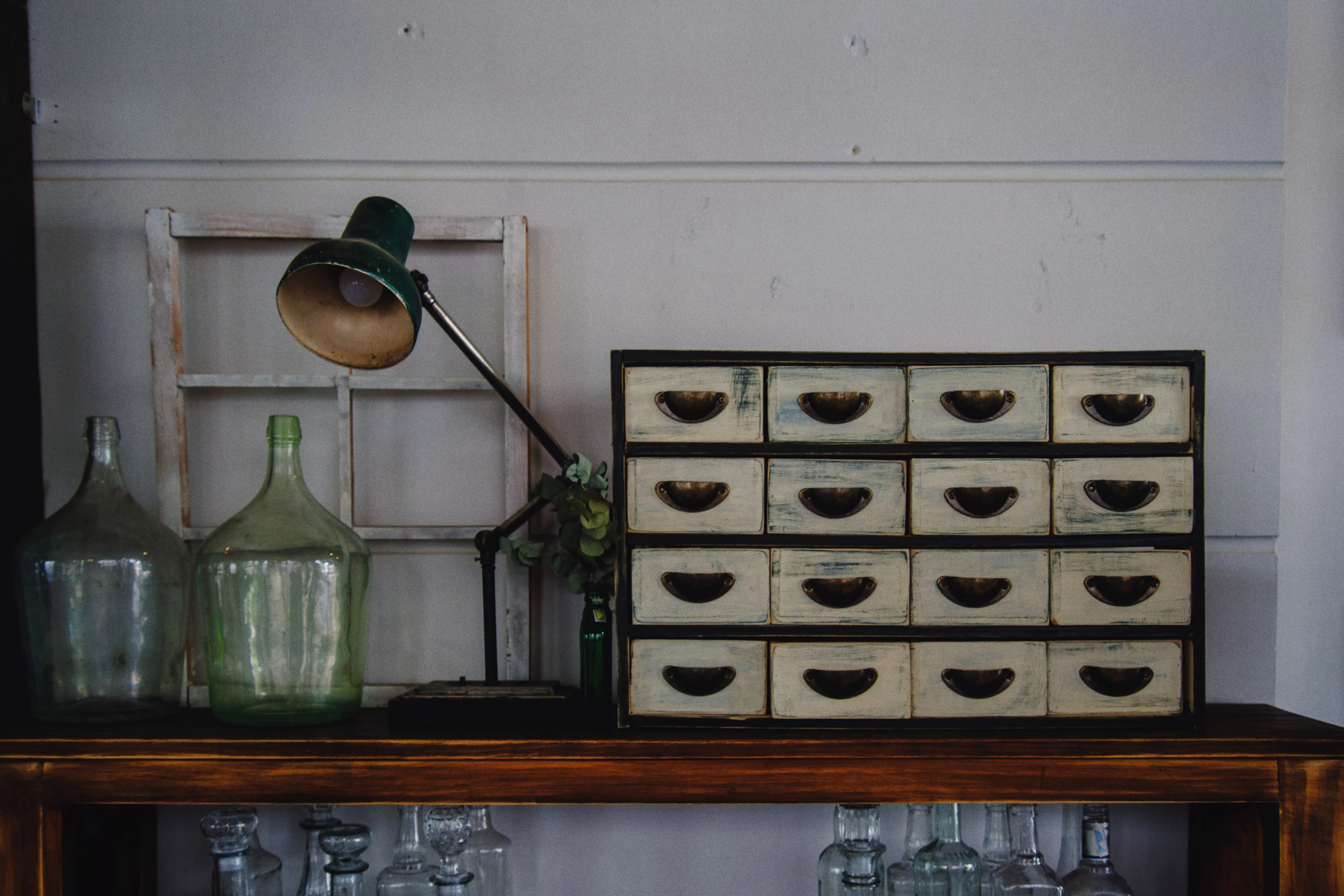 wooden drawer Charming vintage setup with drawers, green glass bottles, and desk lamp.