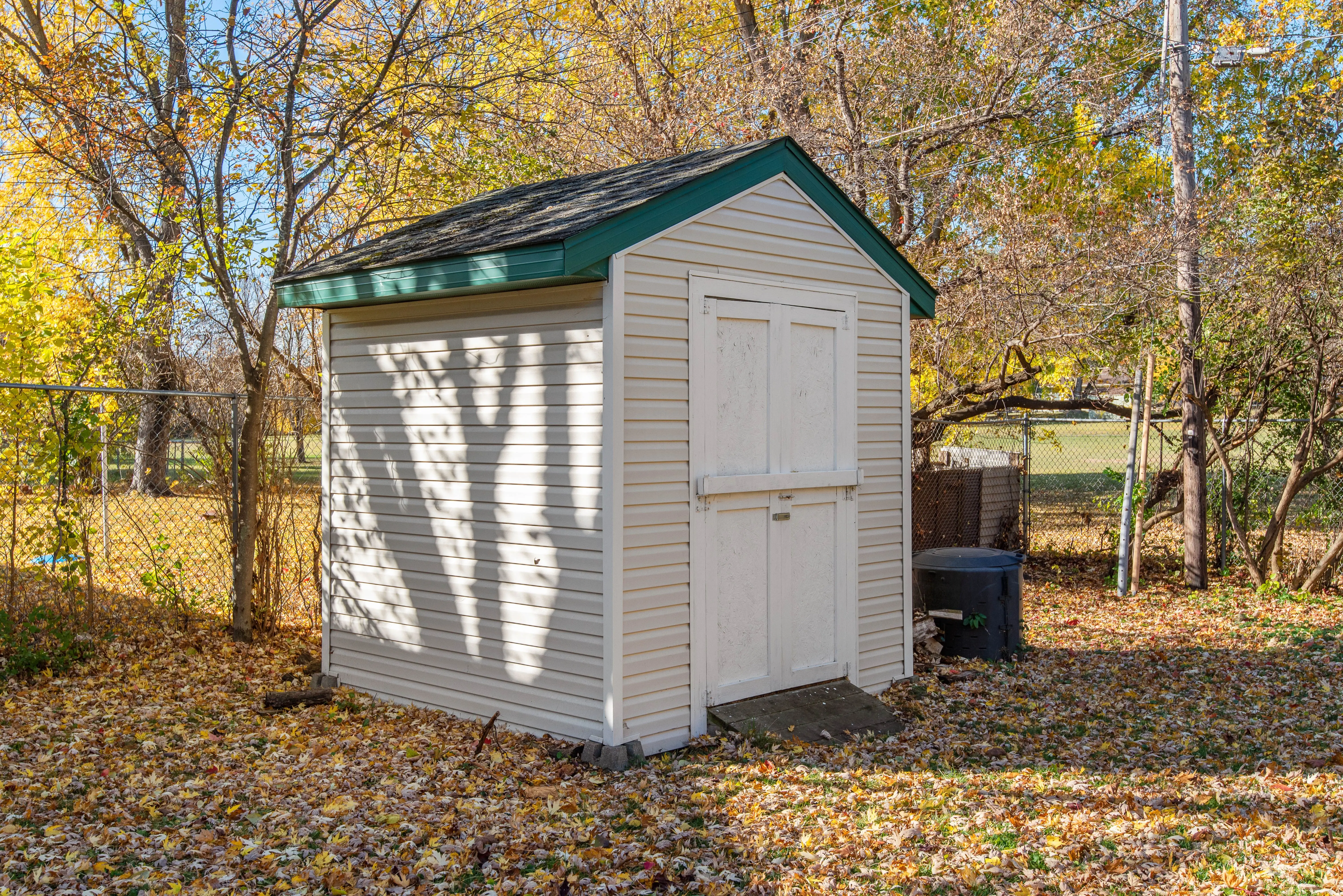 white vinyl siding A quaint backyard shed surrounded by autumn foliage, ideal for storage solutions.