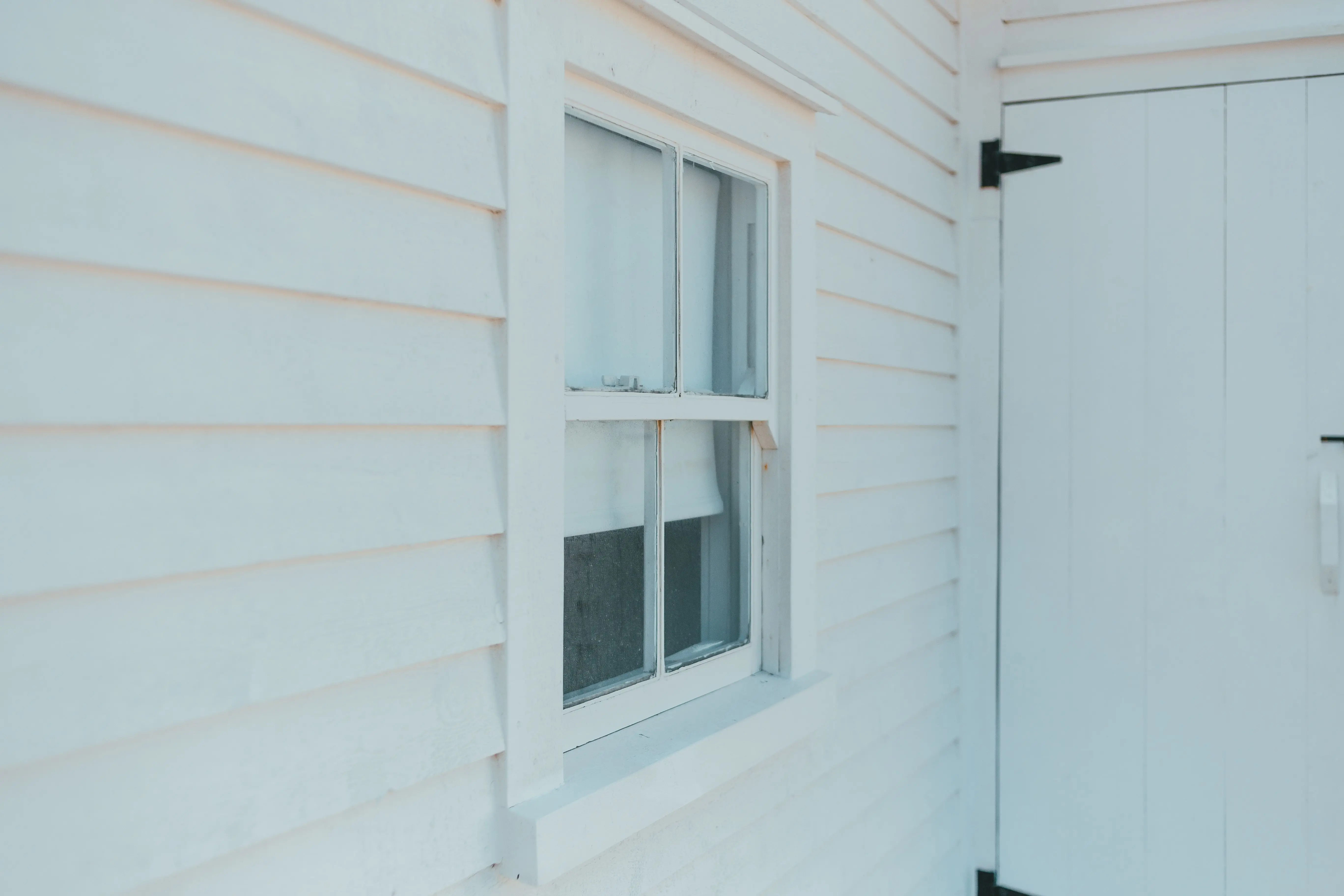 white vinyl siding Close-up of a white wooden facade showcasing a window and door, highlighting minimalist architecture.