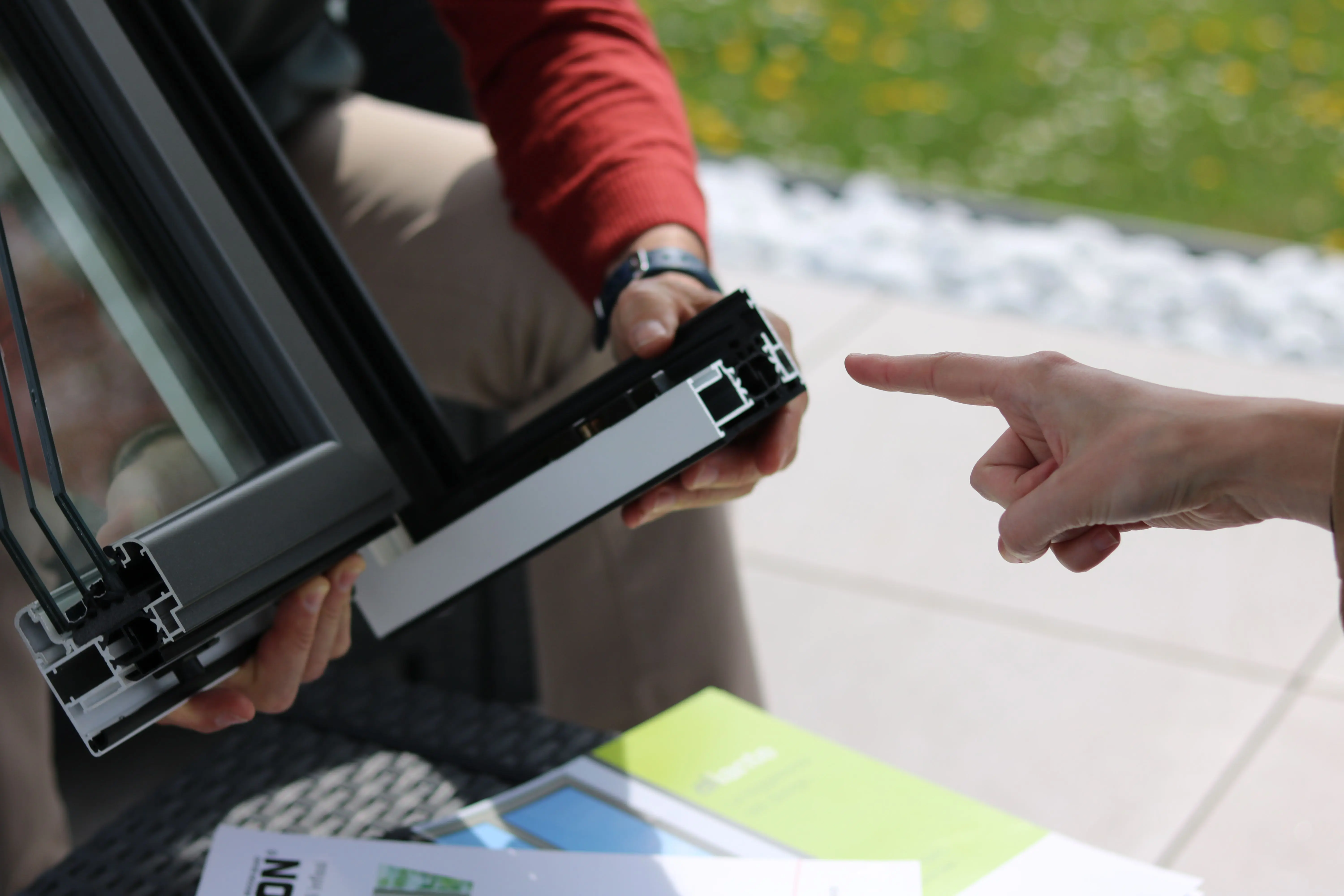 window replacement cost calculator Close-up of two people examining an aluminum window frame outdoors.