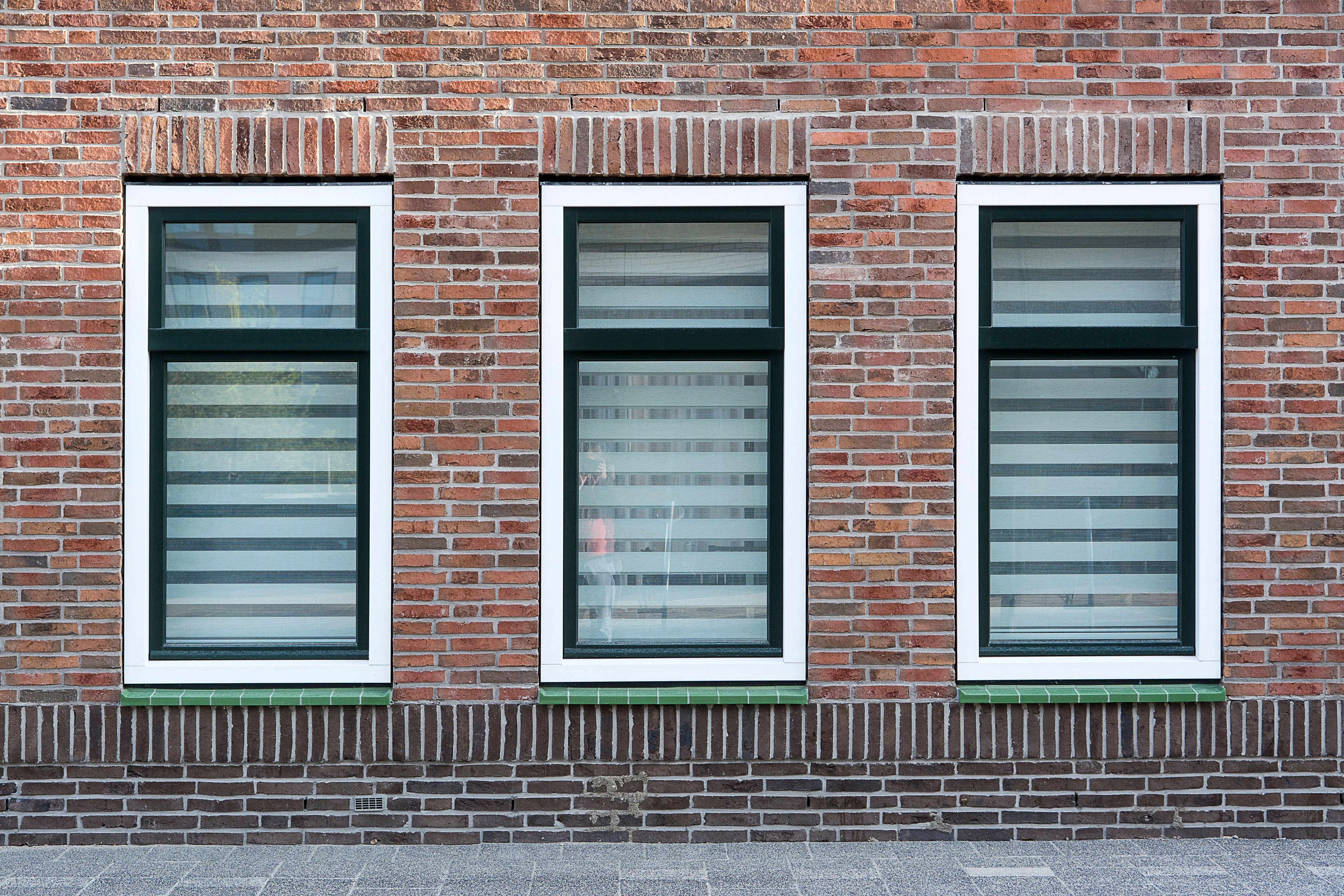 window replacement cost calculator A modern brick wall with three symmetrical windows featuring black and white striped blinds.