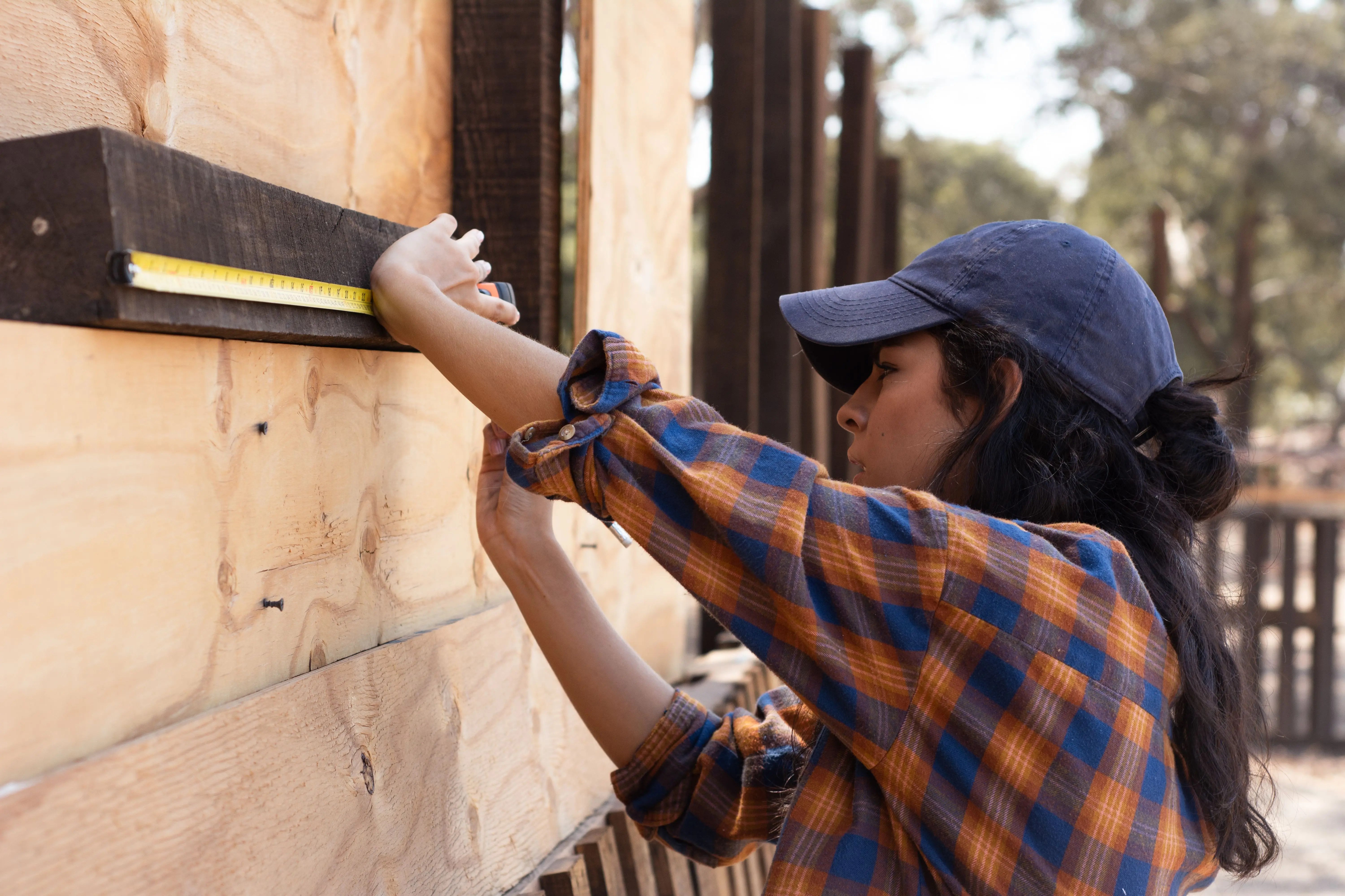 siding installation cost Side view of a woman using a tape measure on wood for an outdoor construction project.