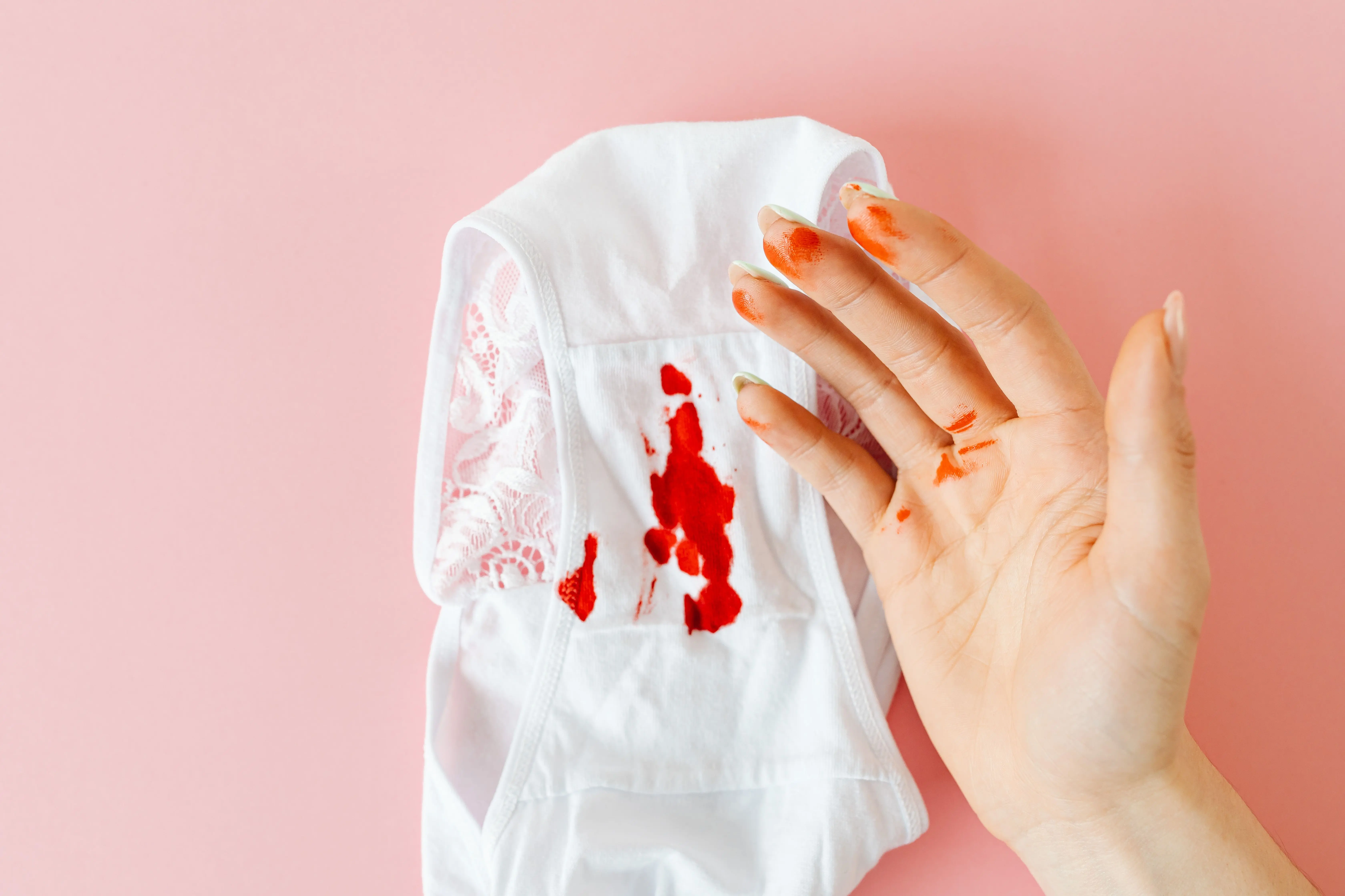 how to get blood stains out of jeans Close-up of a hand with blood stains next to bloodstained underwear on pink background.