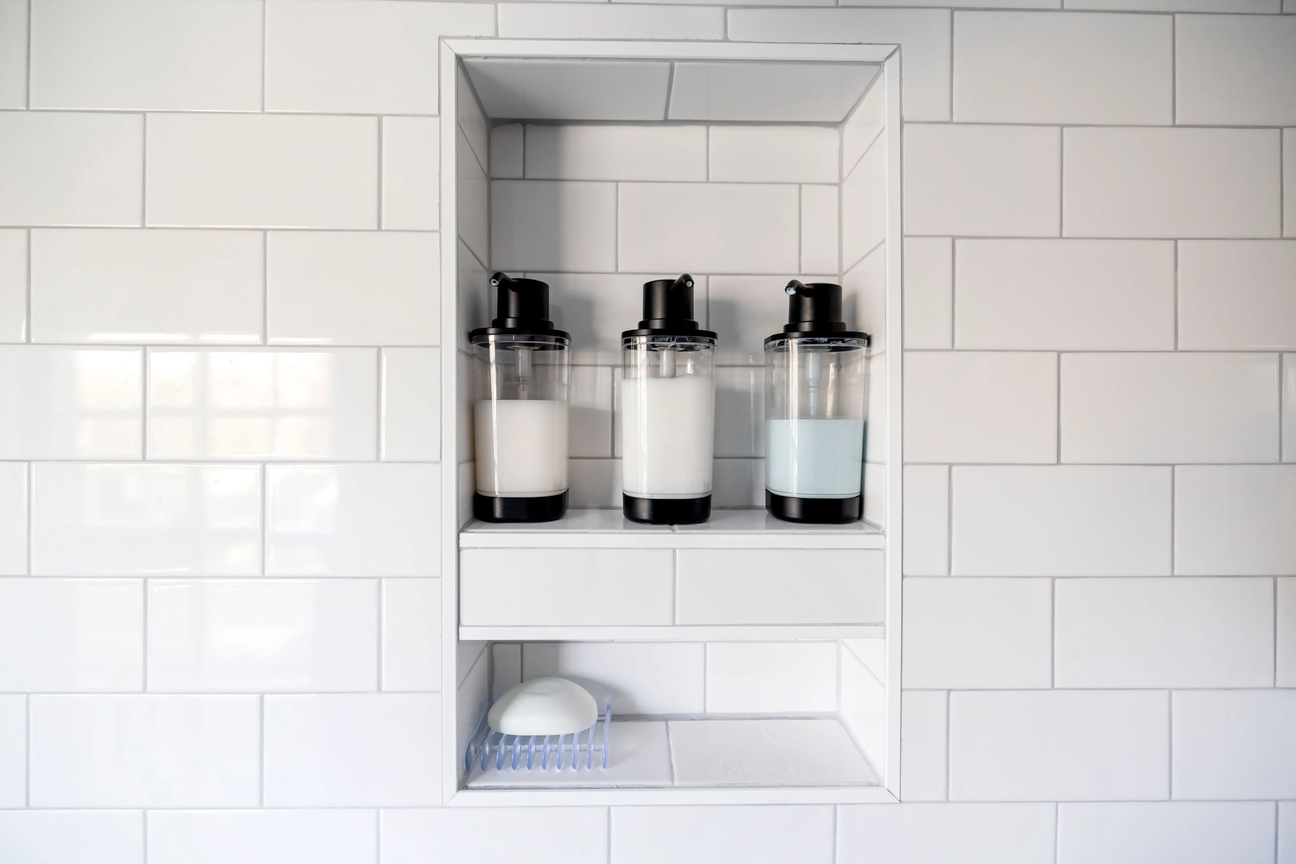 towel shelf Clean and minimalist bathroom design featuring soap dispensers and white tiles.