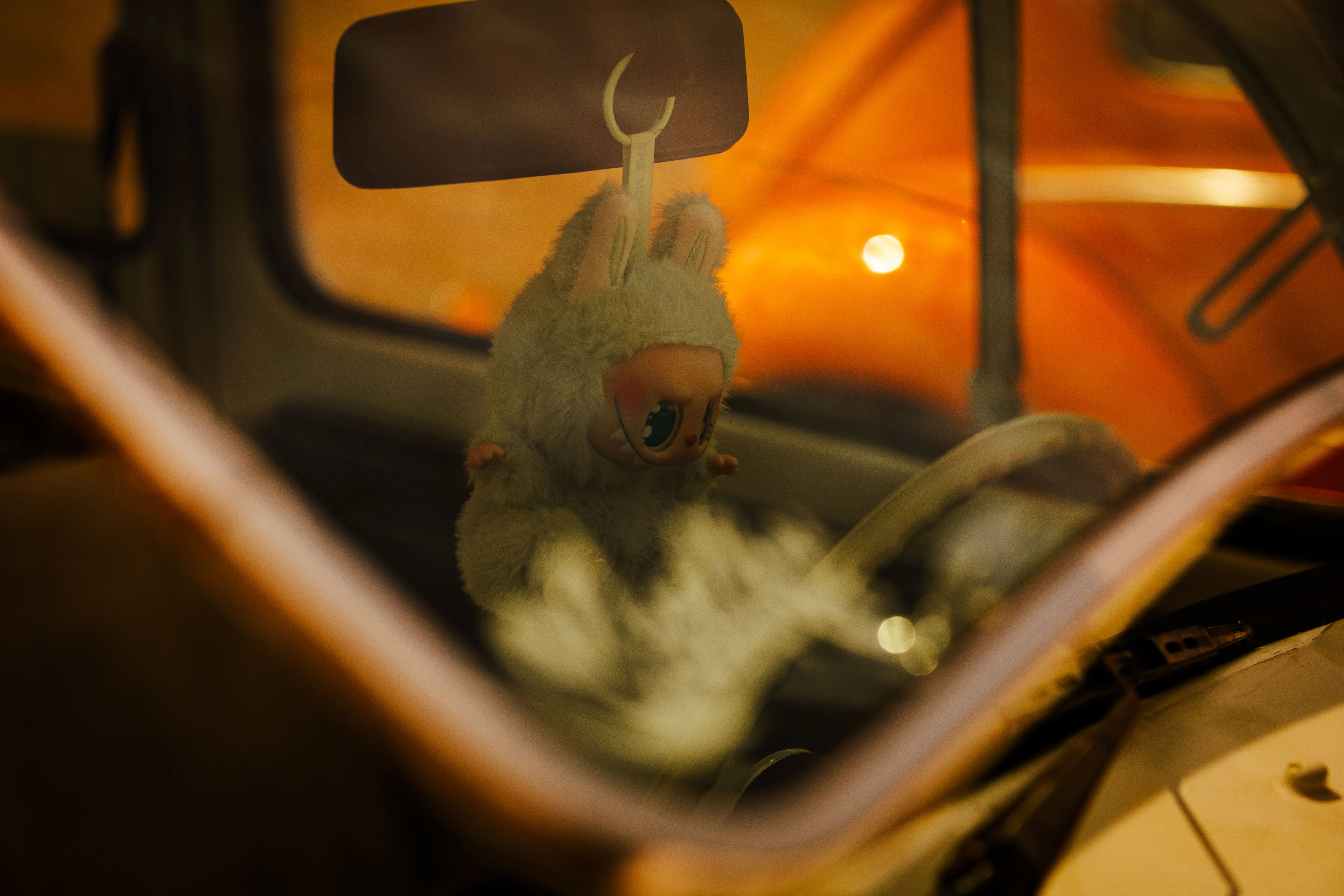 tiny beetles in house A cozy scene inside a vintage car with a cute plush toy hanging from the rearview mirror, captured in São Paulo.