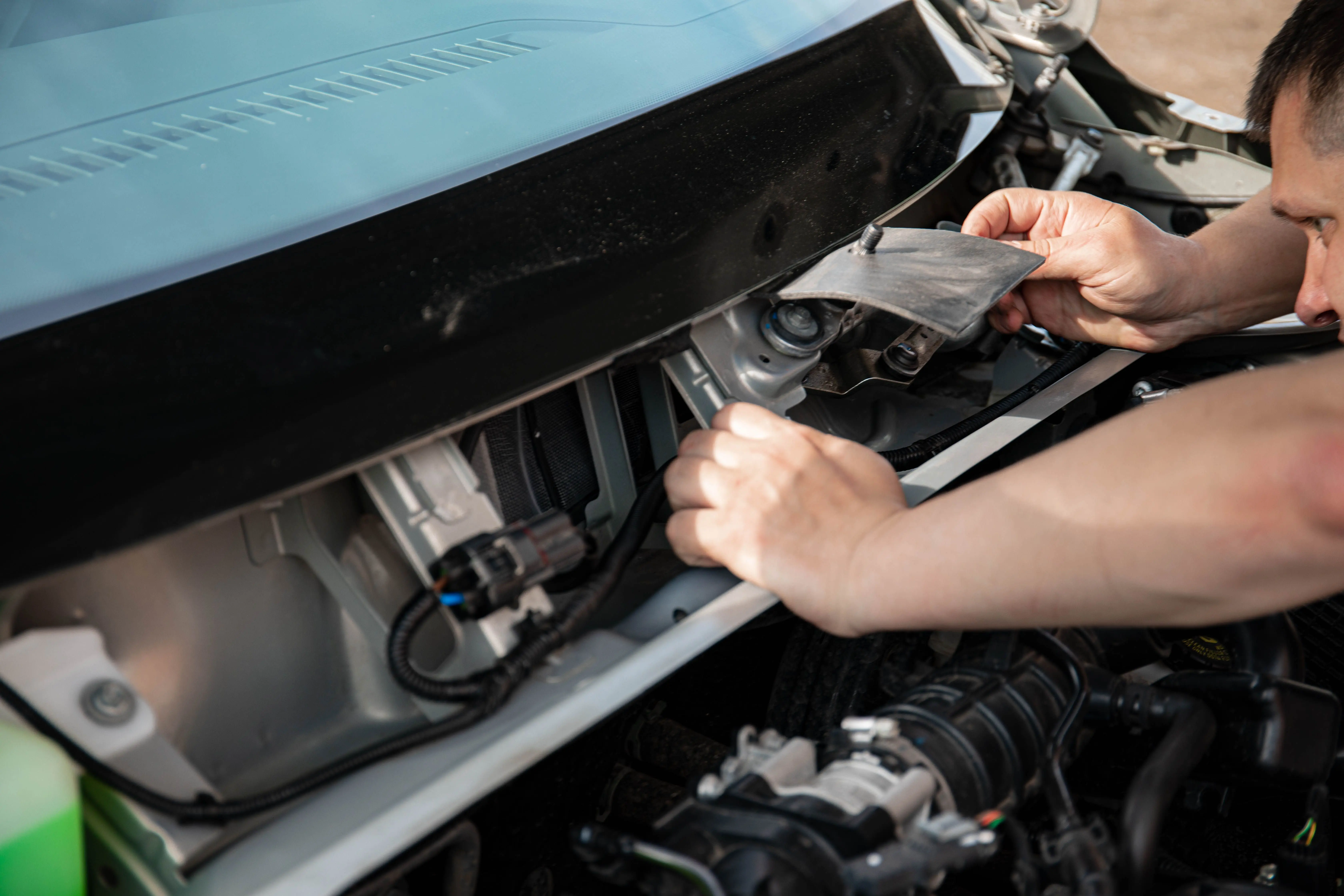 how to fix paint chips on car Close-up of a mechanic working on a car engine outdoors in bright daylight.