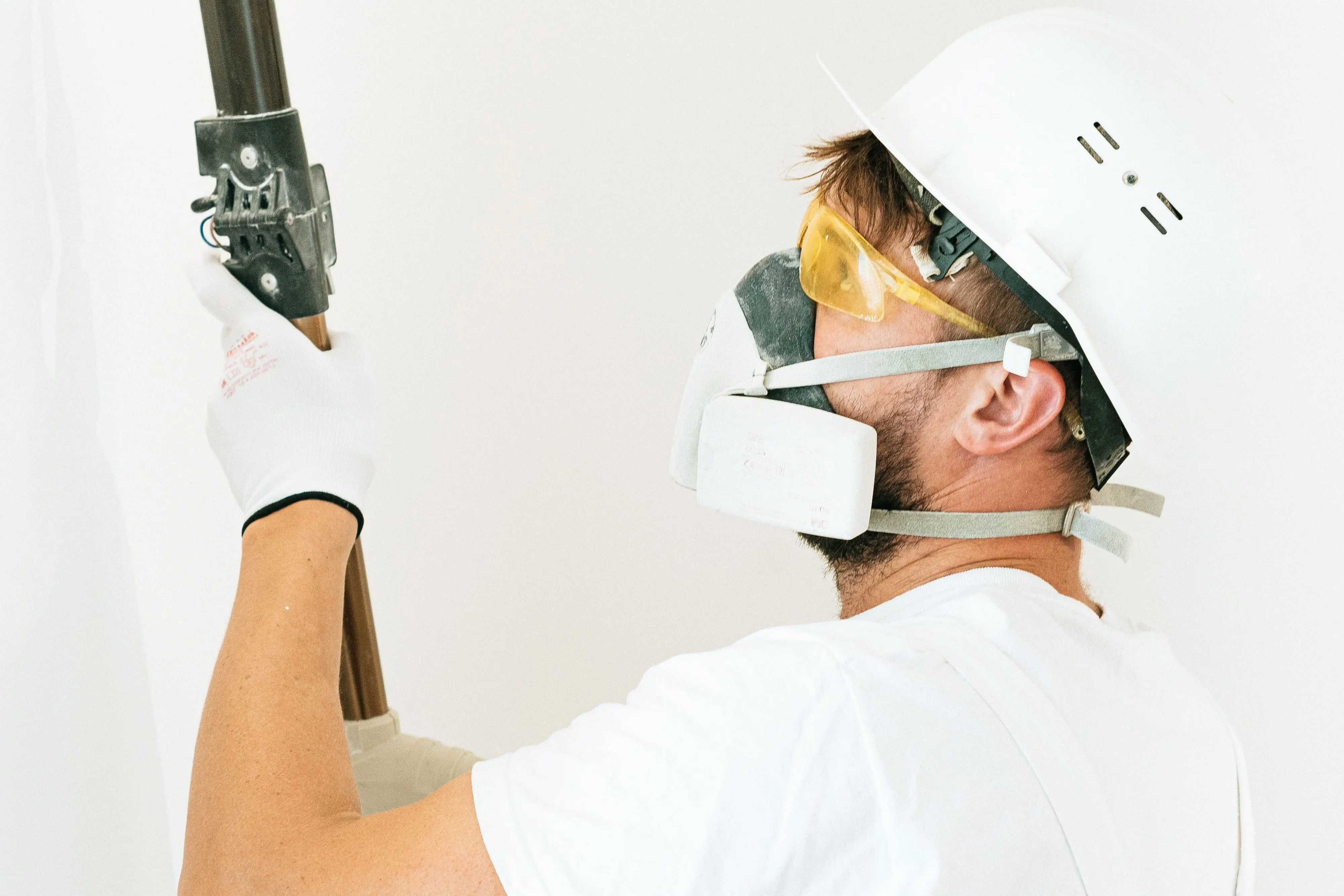 siding installation cost Construction worker wearing safety gear applying paint with a roller indoors. Focus on safety measures.