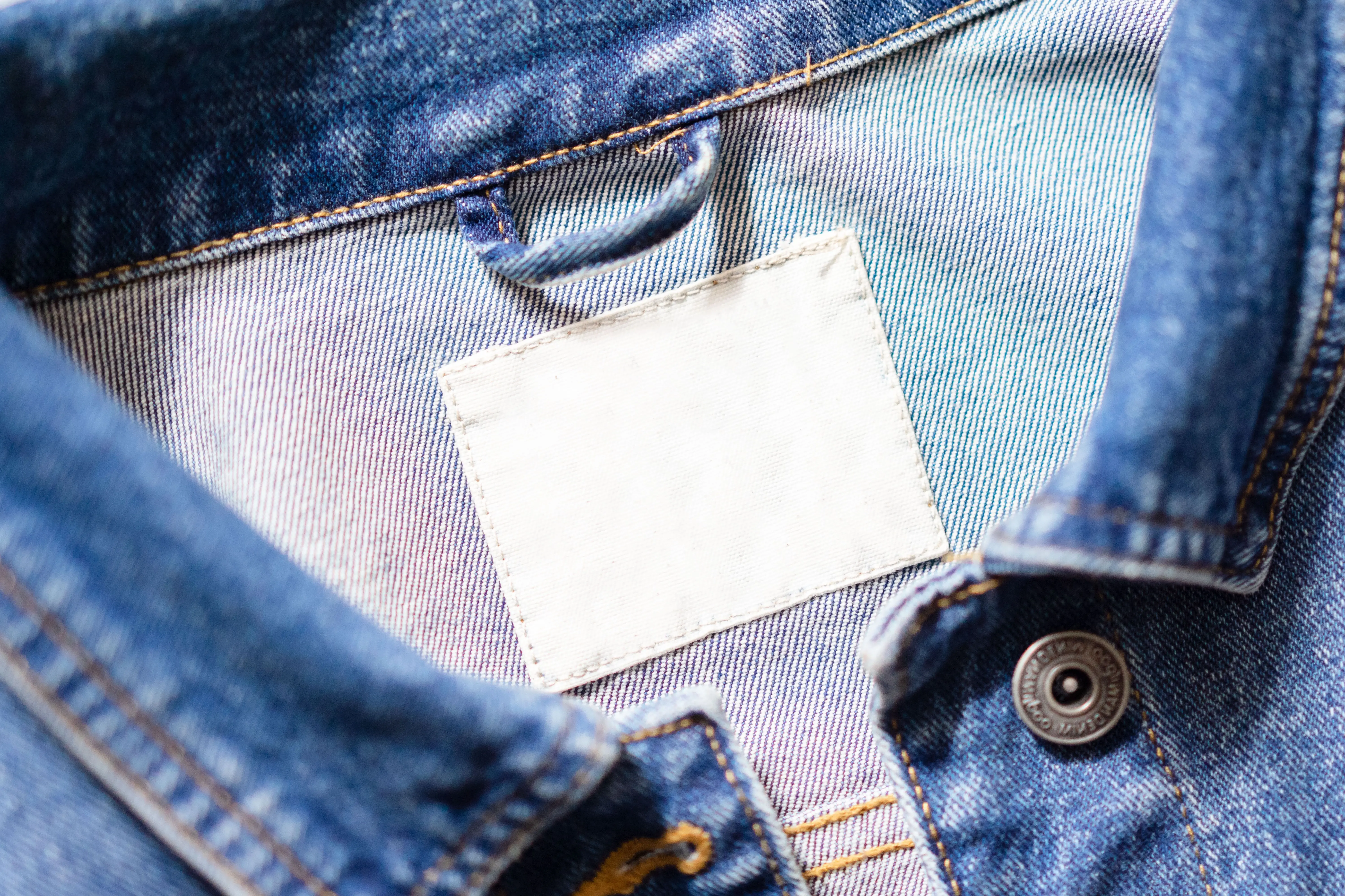 how to get blood out of denim Close-up shot of a denim jacket's collar featuring a blank white tag and detailed stitching.