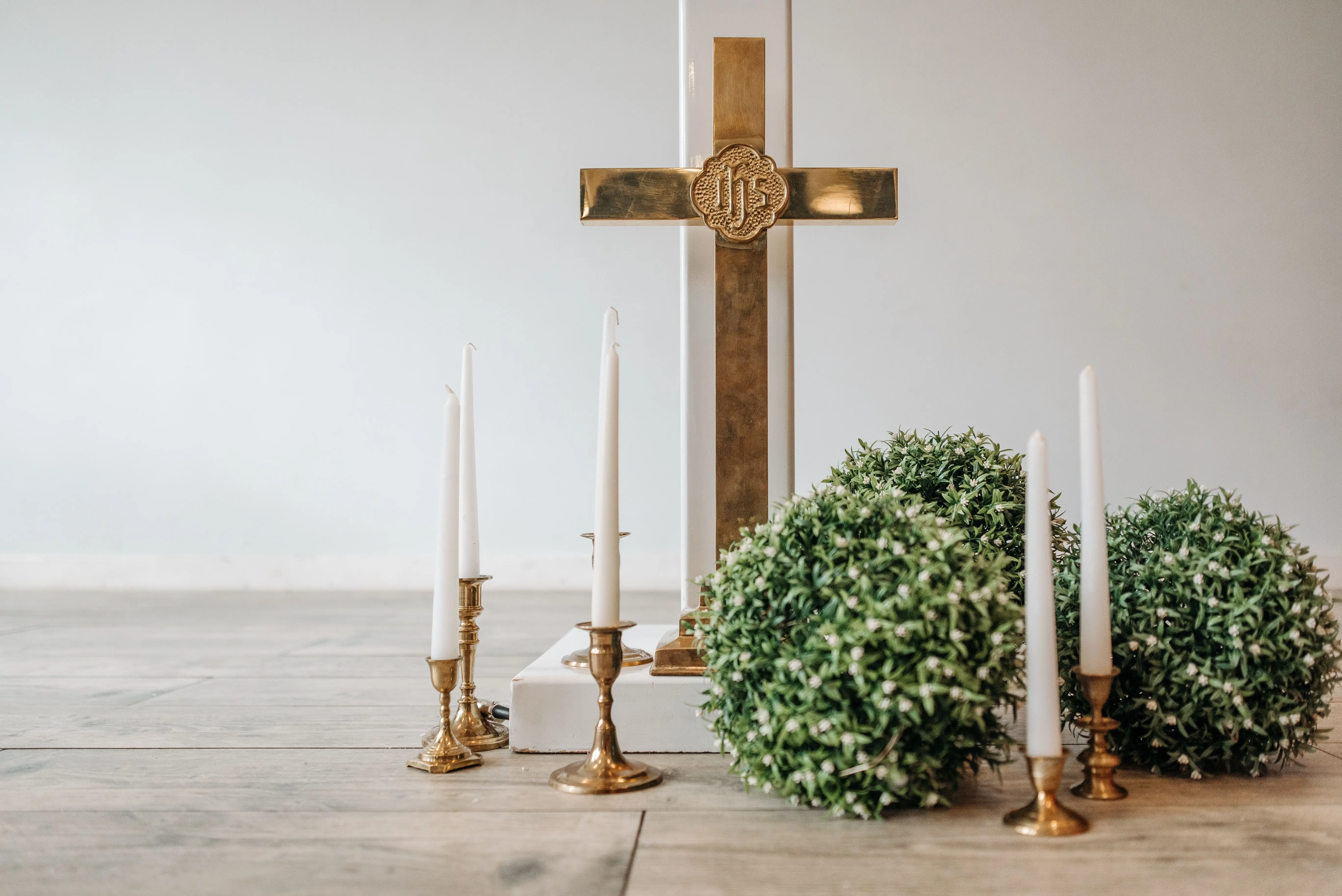 tapered candle holders A gold cross with taper candles and greenery on a wooden floor.