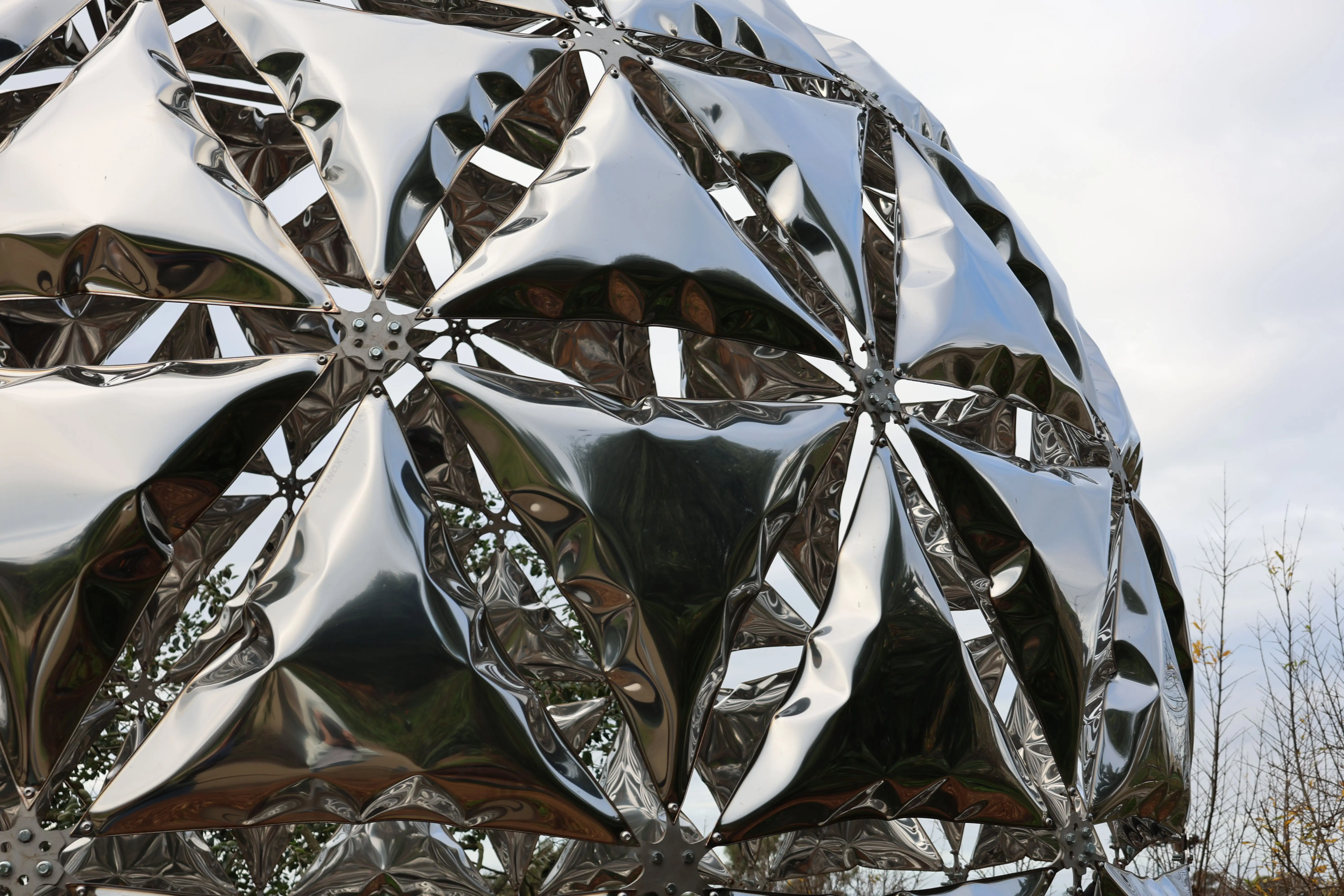 large exterior metal wall art A modern metallic geodesic dome sculpture reflecting the sky, photographed outdoors.