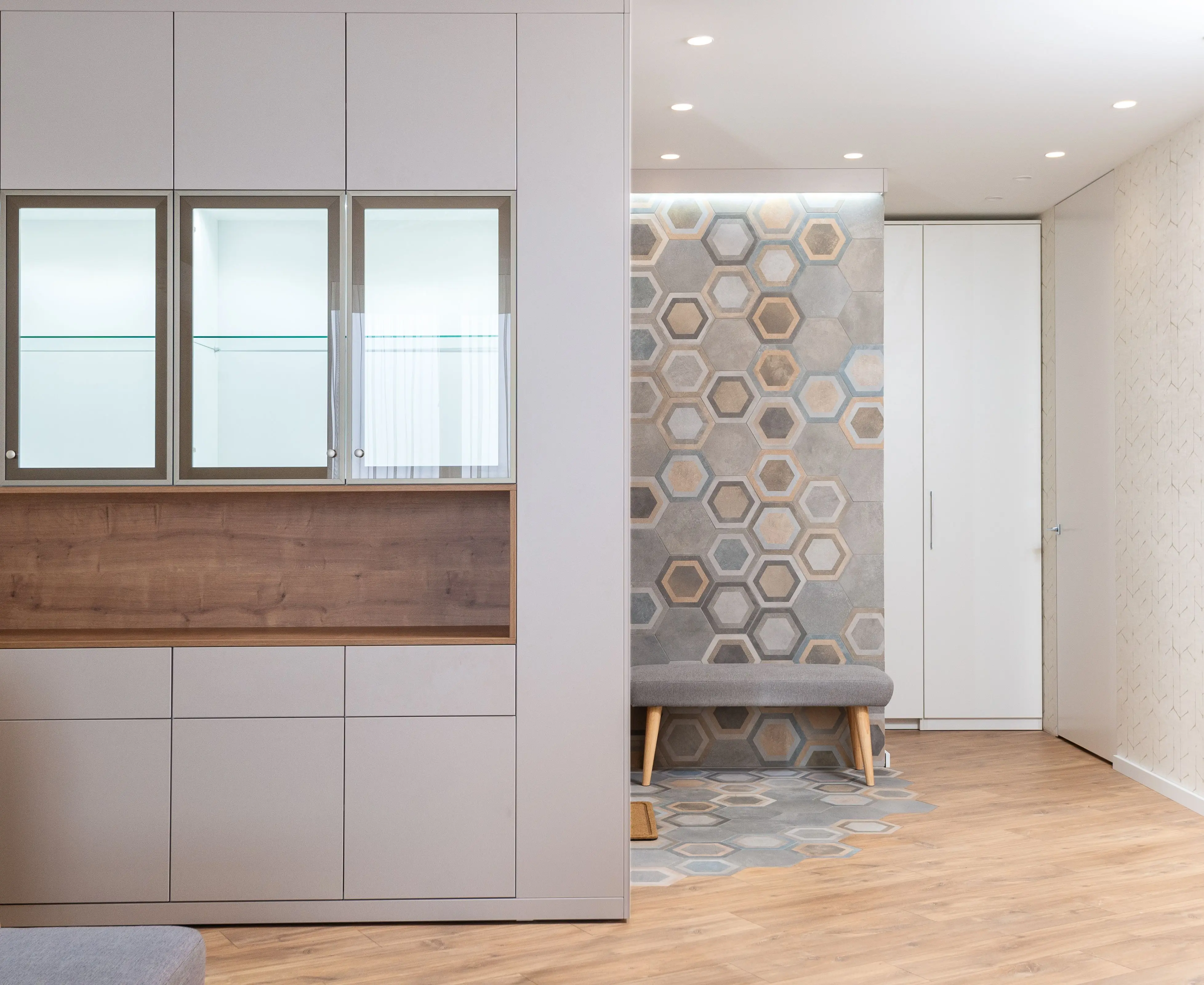 paint inspo Glass cabinets in white kitchen against modern hallway with fabric bench and wall with hexagonal ornament
