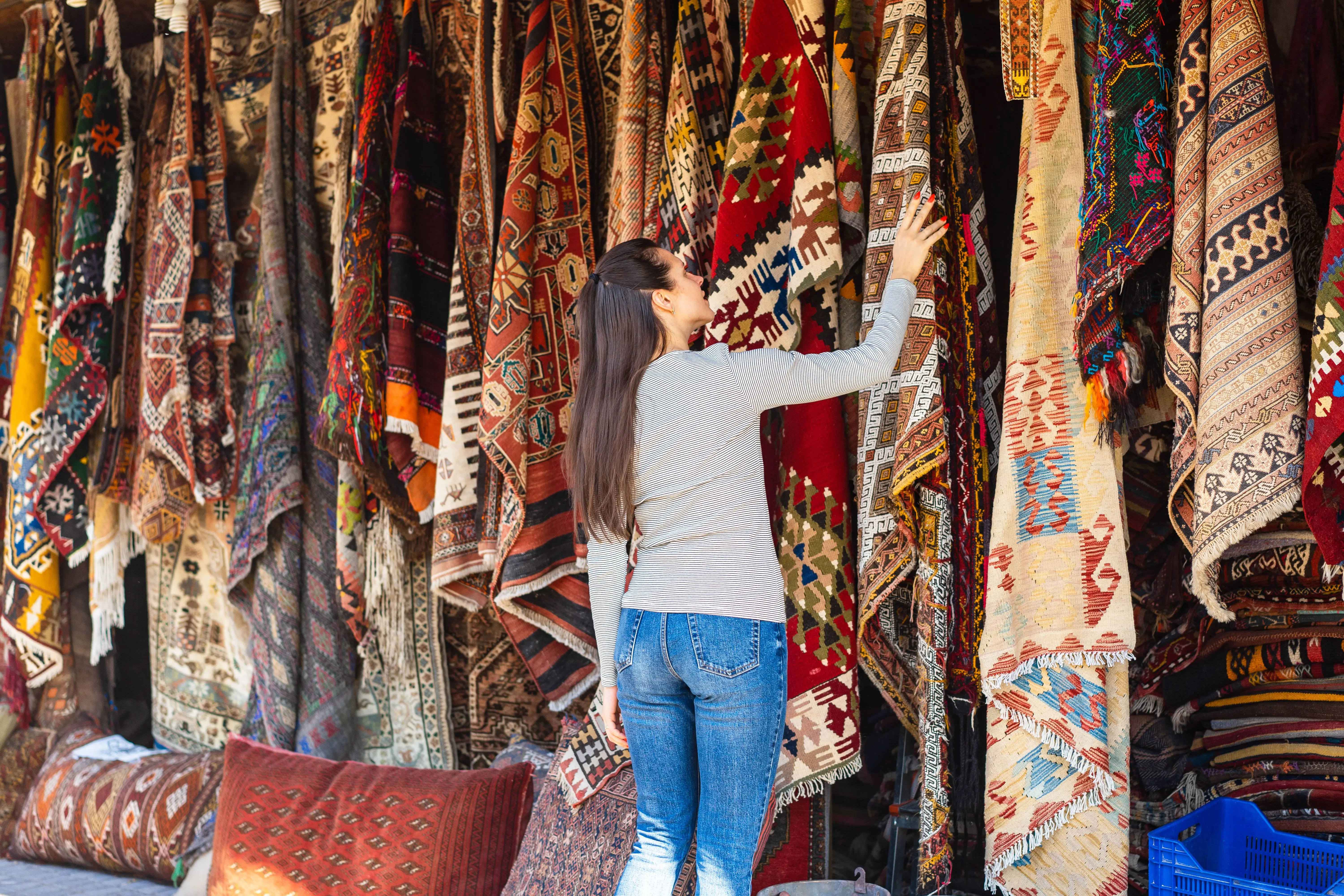 what do fleas look like to the human eye A woman with long hair touches vibrant carpets at a textile stall, admiring the intricate patterns.