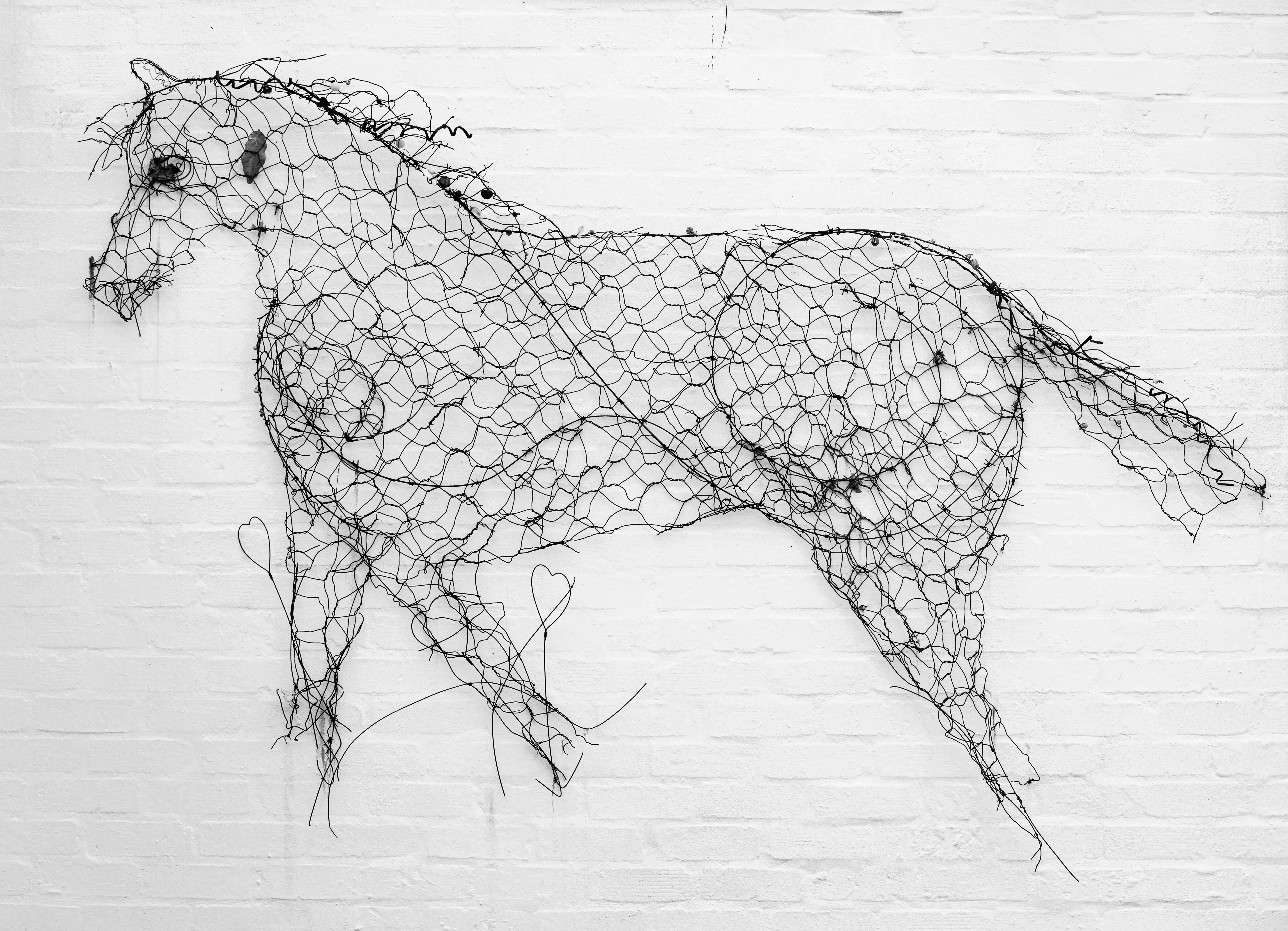 large exterior metal wall art Artistic wire horse sculpture mounted on a white brick wall. Unique and creative design.