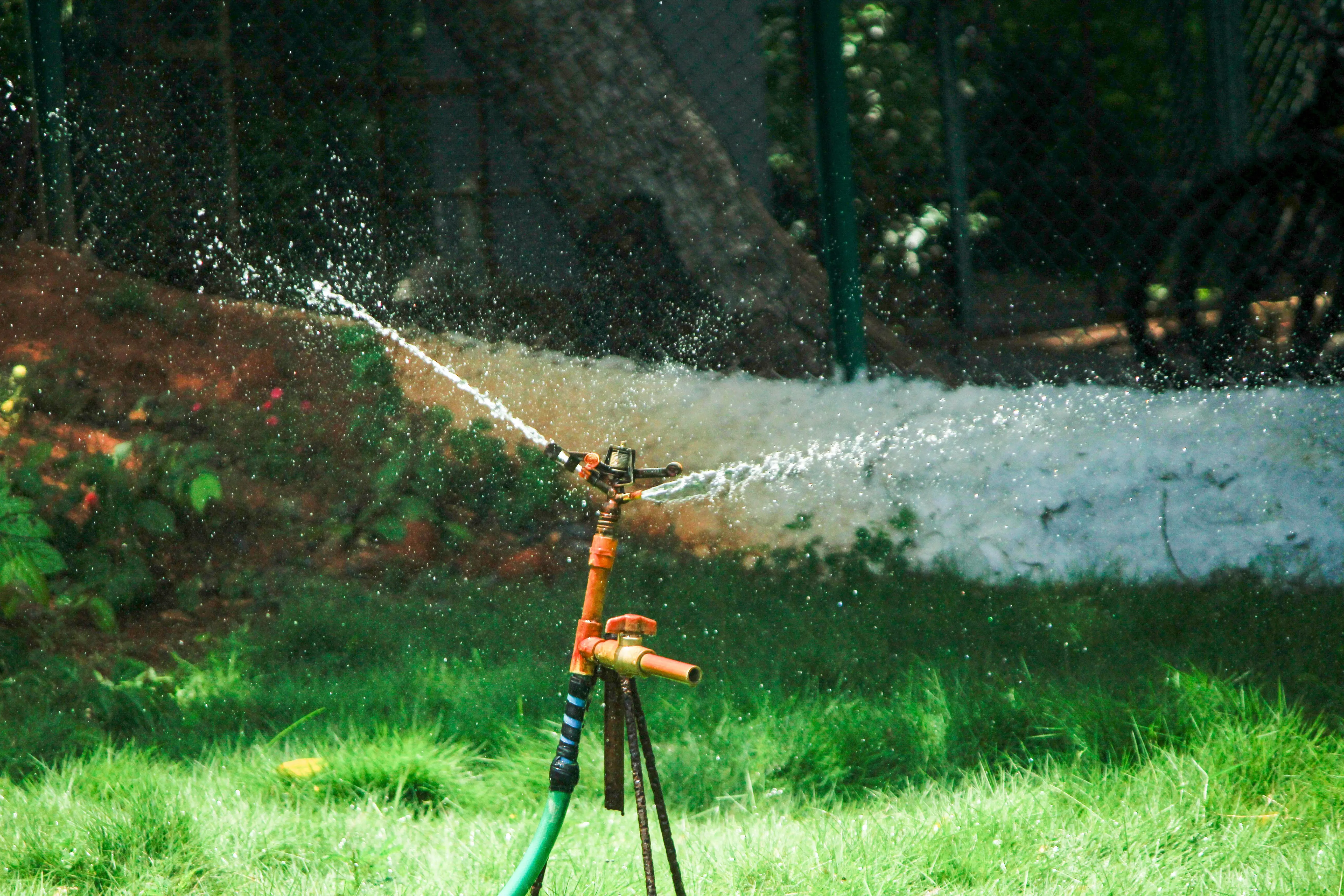 self watering garden A garden sprinkler irrigating a lush green lawn, creating a refreshing outdoor scene.