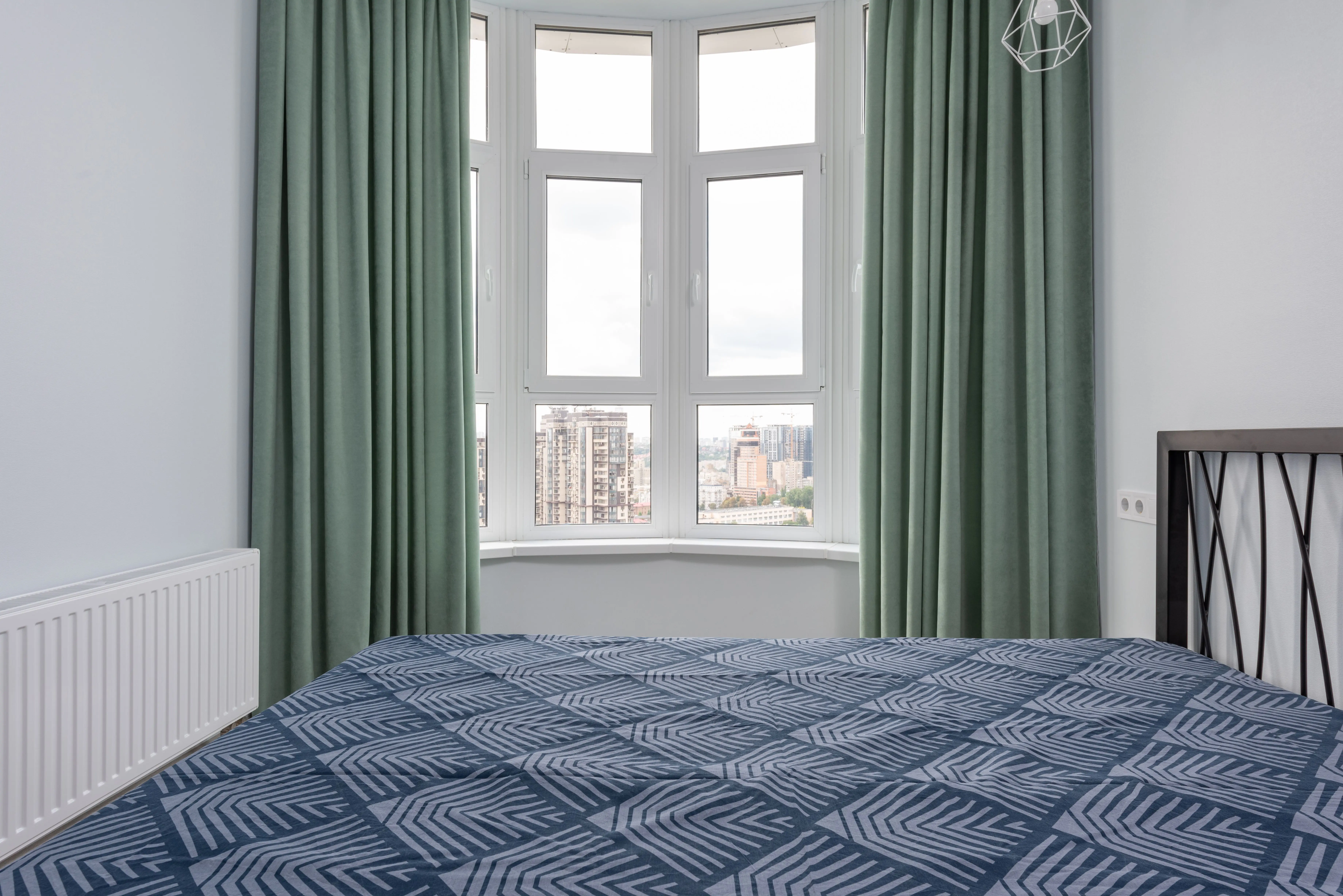 patterned drapes Interior of cozy light bedroom with blue blanket on bed placed against window with green curtain and white walls at home