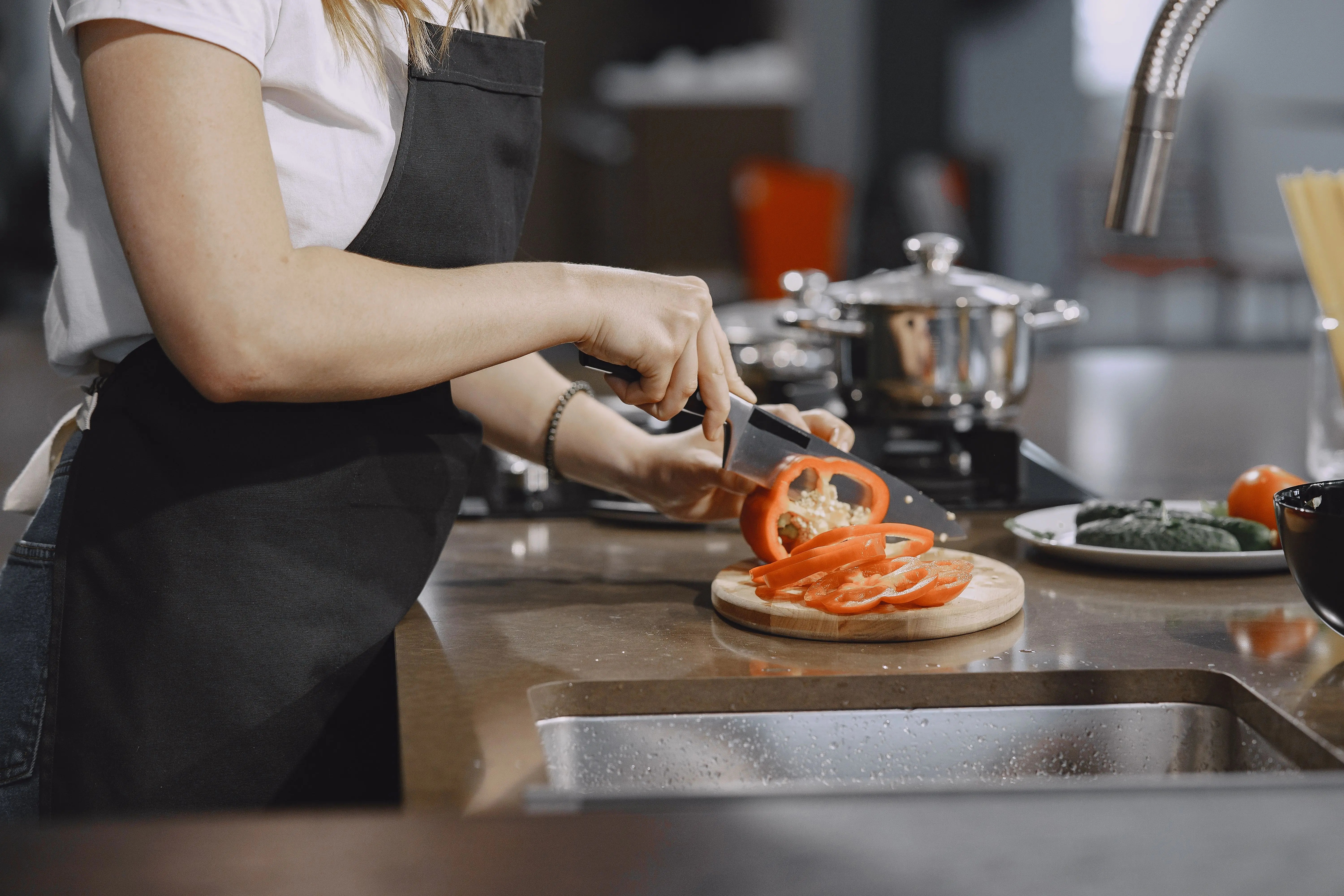 kitchen work table Woman slicing tomatoes in a modern kitchen setting with cooking equipment on the counter.