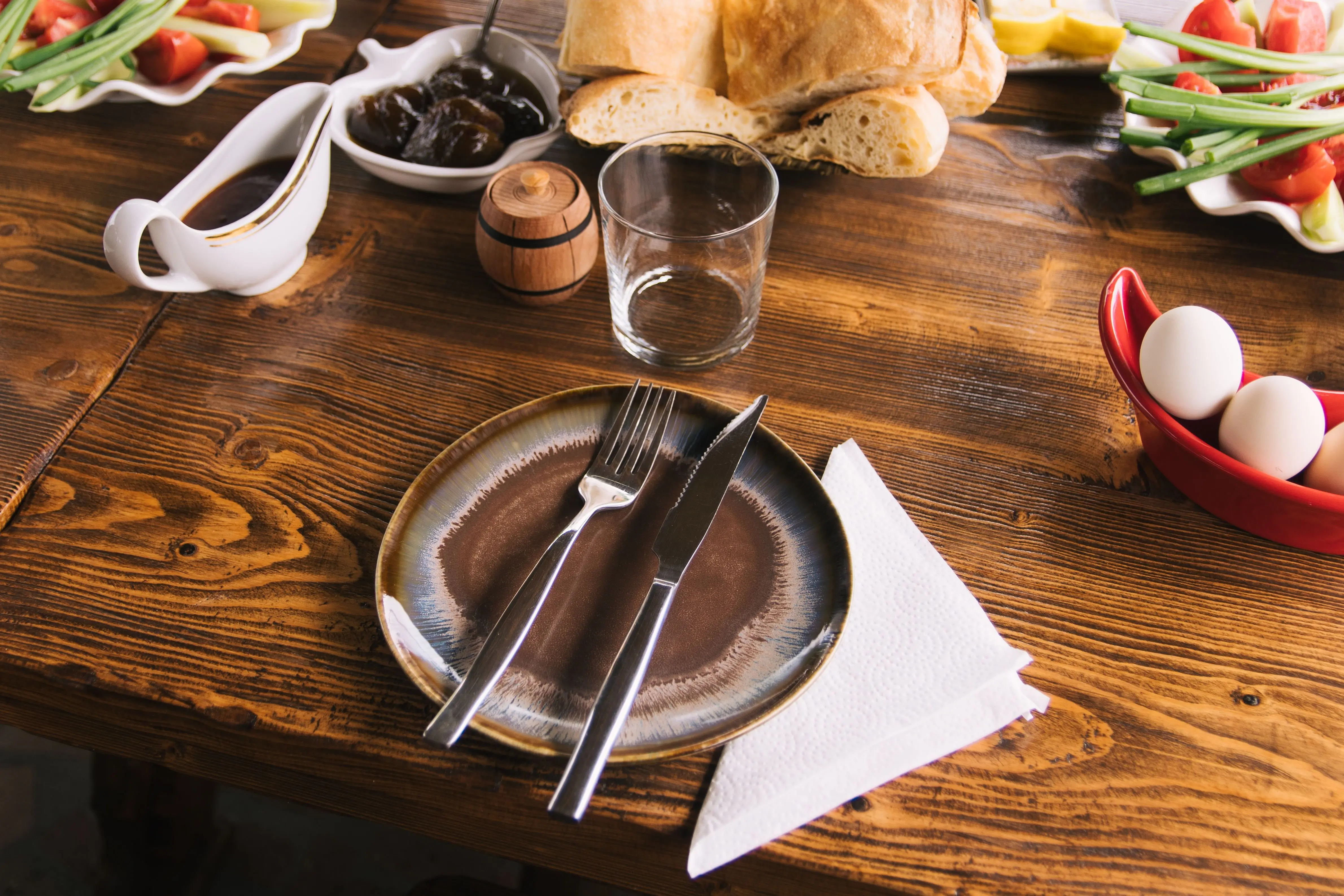 kitchen work table A rustic table setup with bread, veggies, and a ceramic plate for a cozy meal.