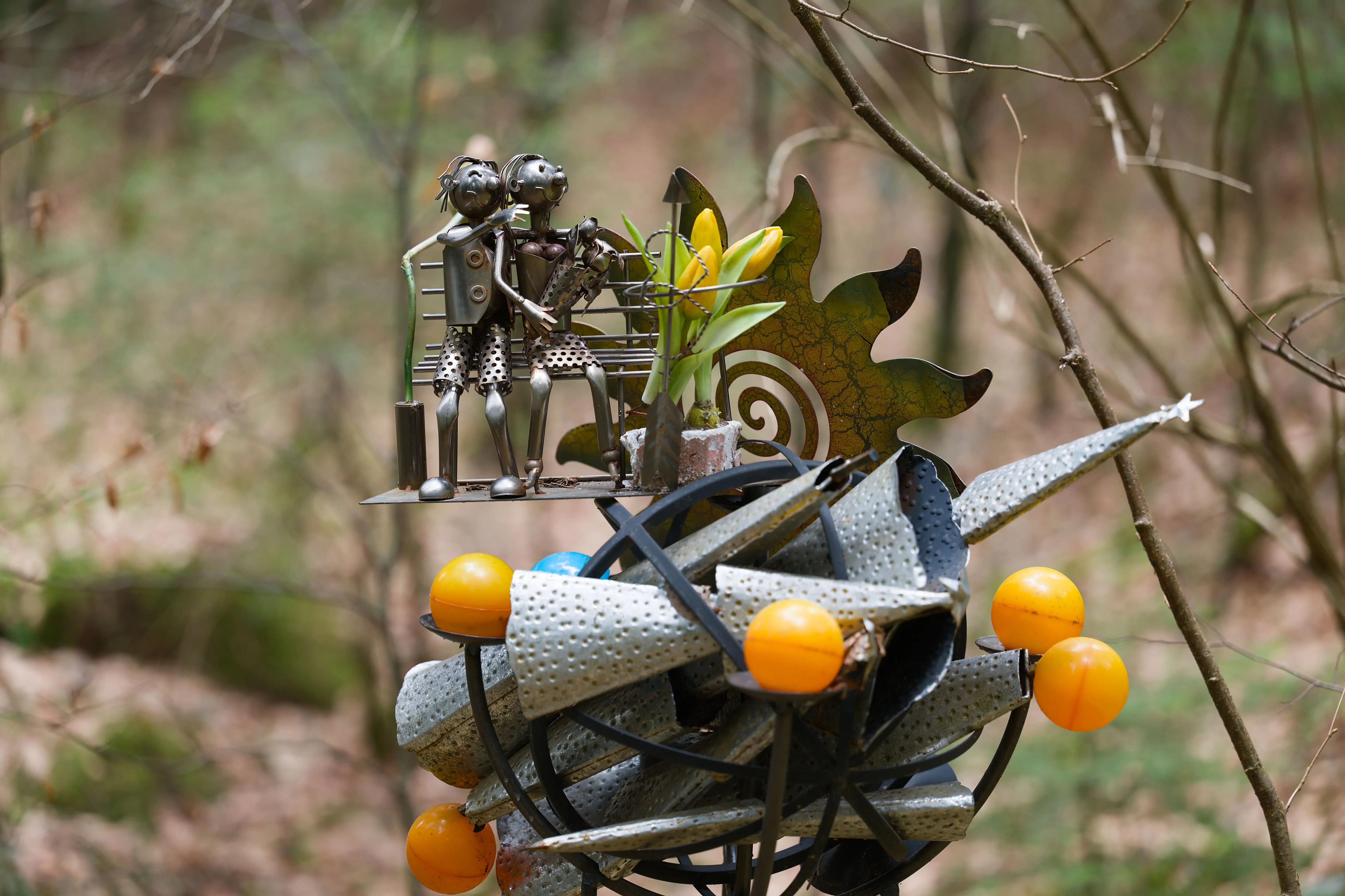 outdoor wall decorations metal Metal sculpture with whimsical figures and plants in a serene forest environment.