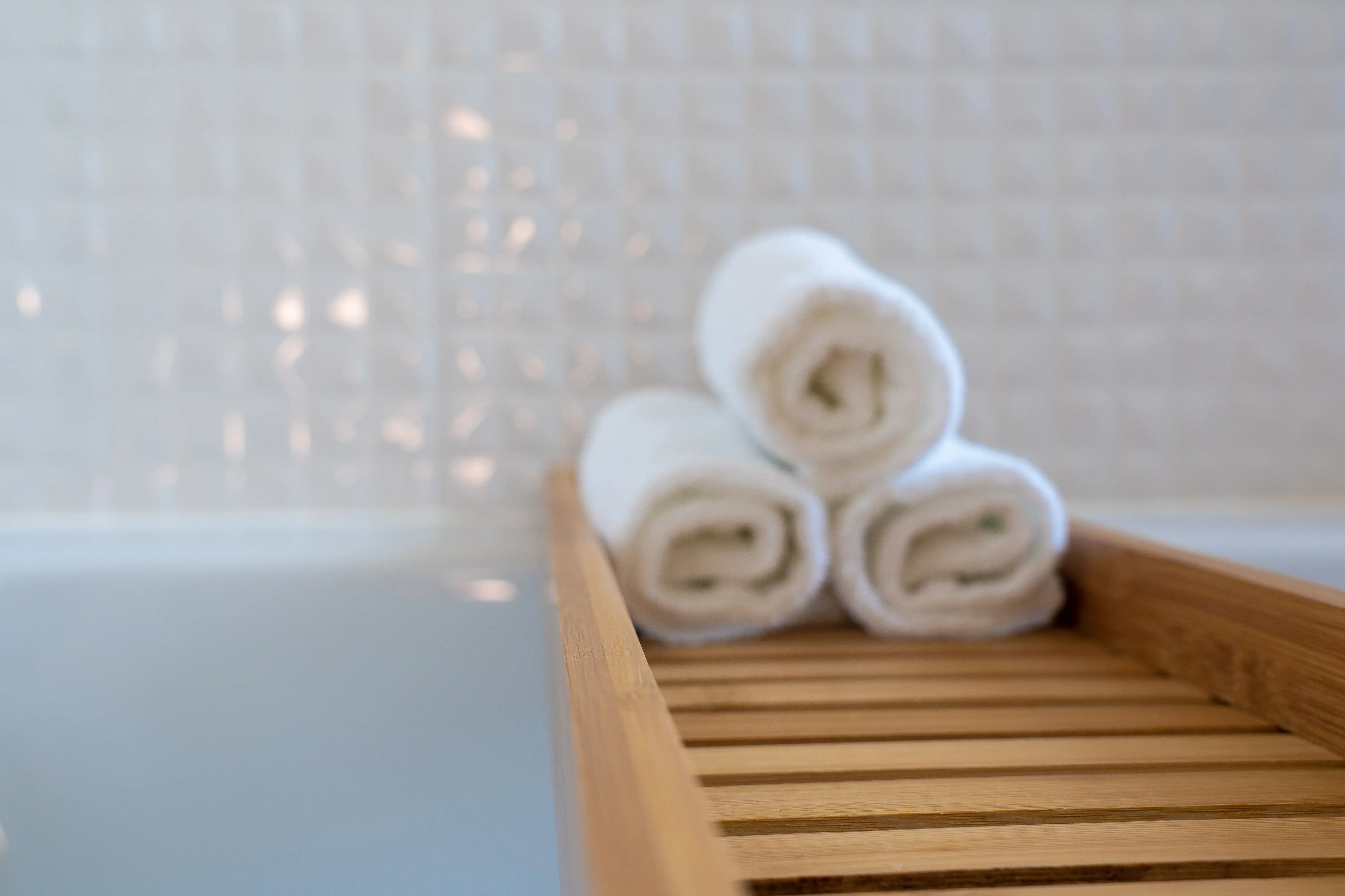 luxury home renovations A close-up of rolled white towels on a wooden bath tray in a modern bathroom.