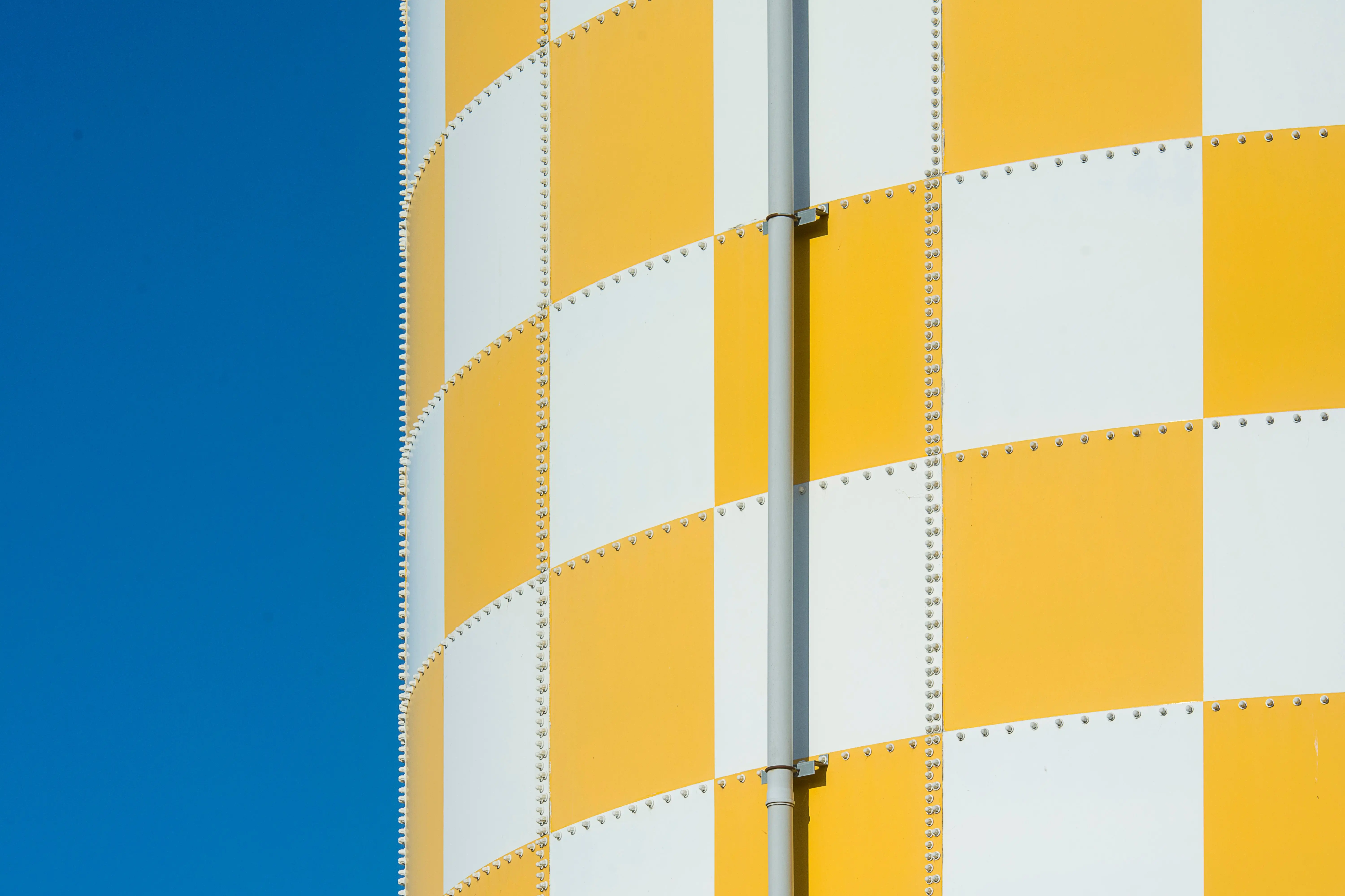 large exterior metal wall art Close-up view of a yellow and white checkered structure with a blue sky backdrop.