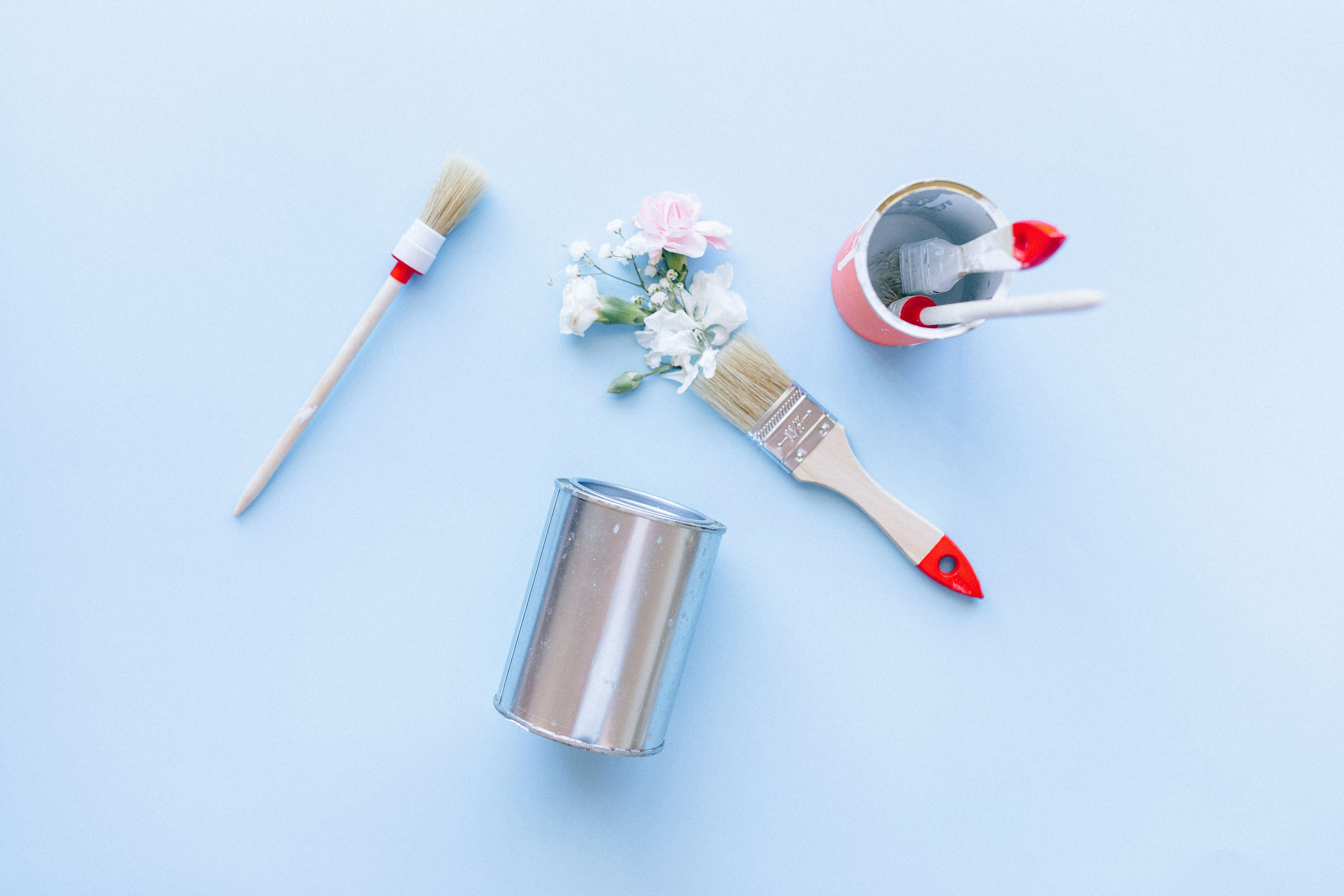 paint inspo Creative top view of paintbrushes, cans, and flowers against a light blue background.