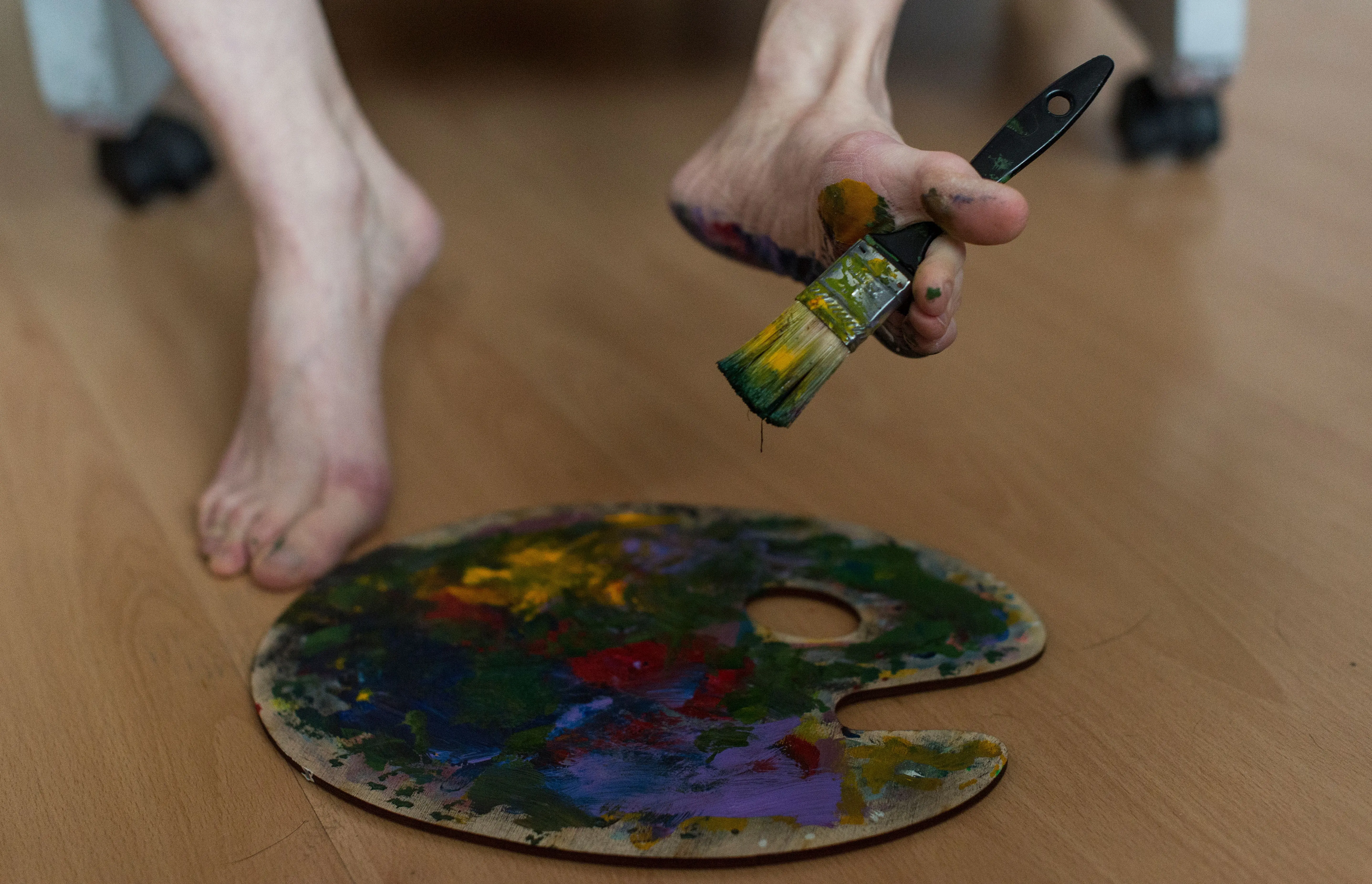 painting price per square foot Close-up of feet holding a paintbrush with a colorful palette on the floor.