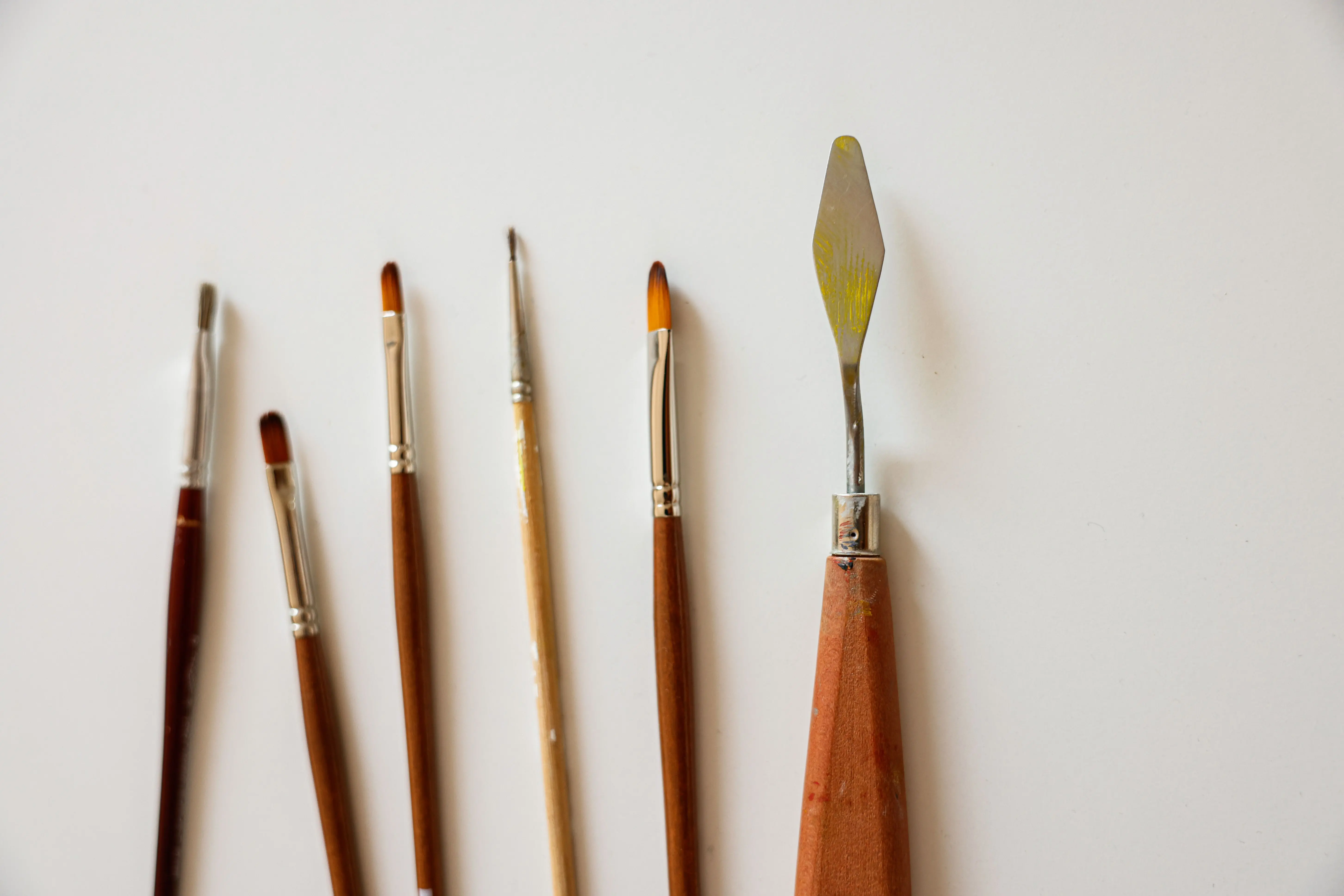 painting price per square foot Lineup of paint brushes and a palette knife on a neutral background.
