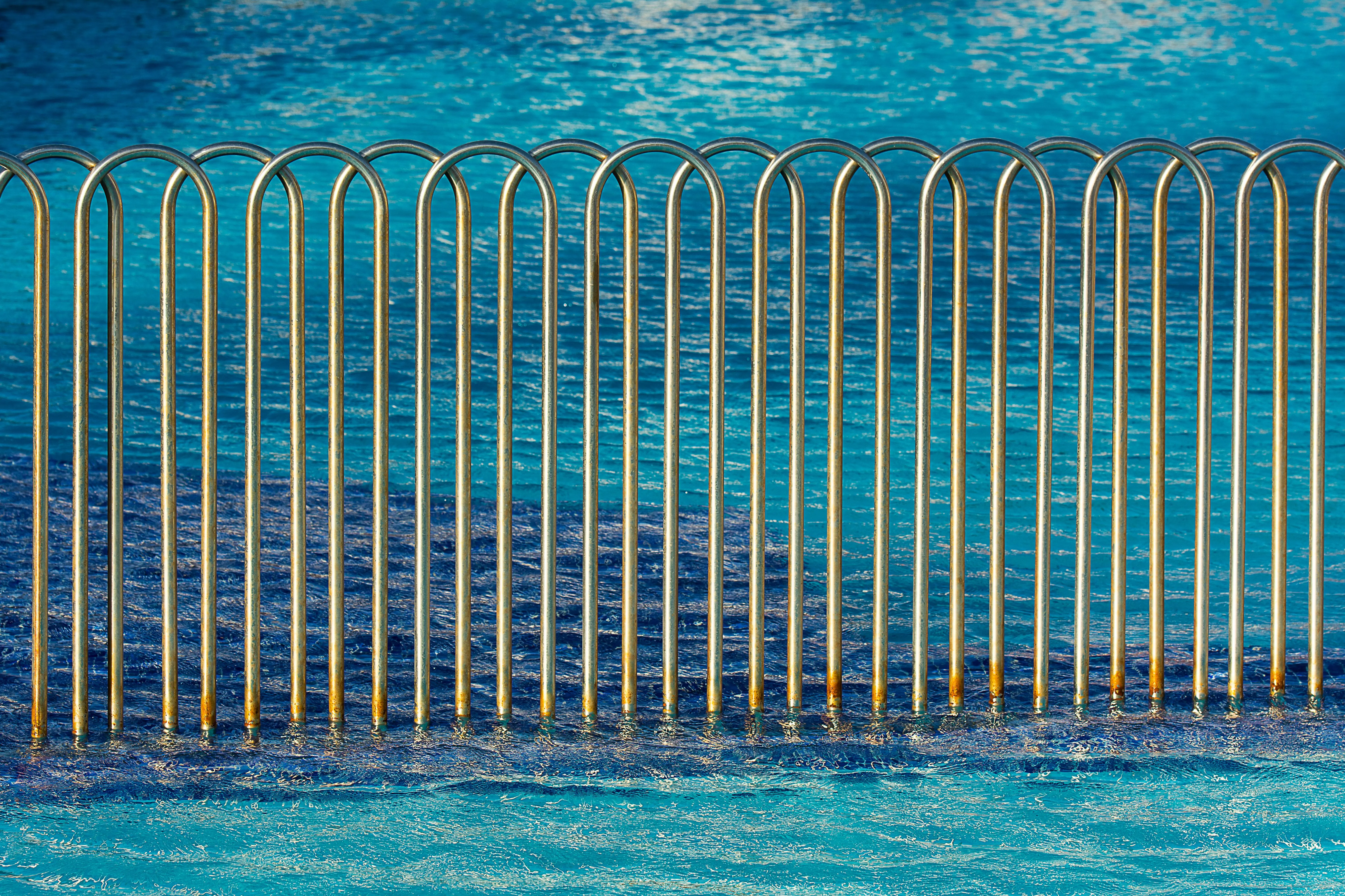 pool gates Modern metal fence with wave pattern beside a clear blue swimming pool, creating a serene aquatic backdrop.
