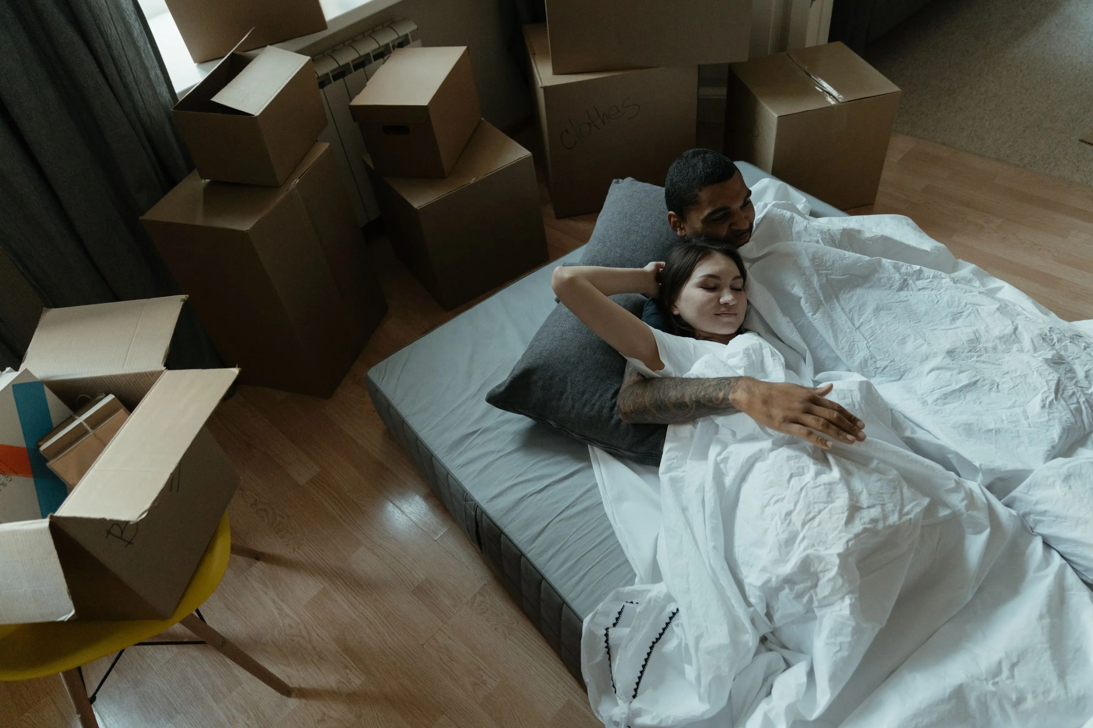 queen bed storage bed A couple relaxing on a mattress surrounded by moving boxes in their new home, embracing a fresh start.