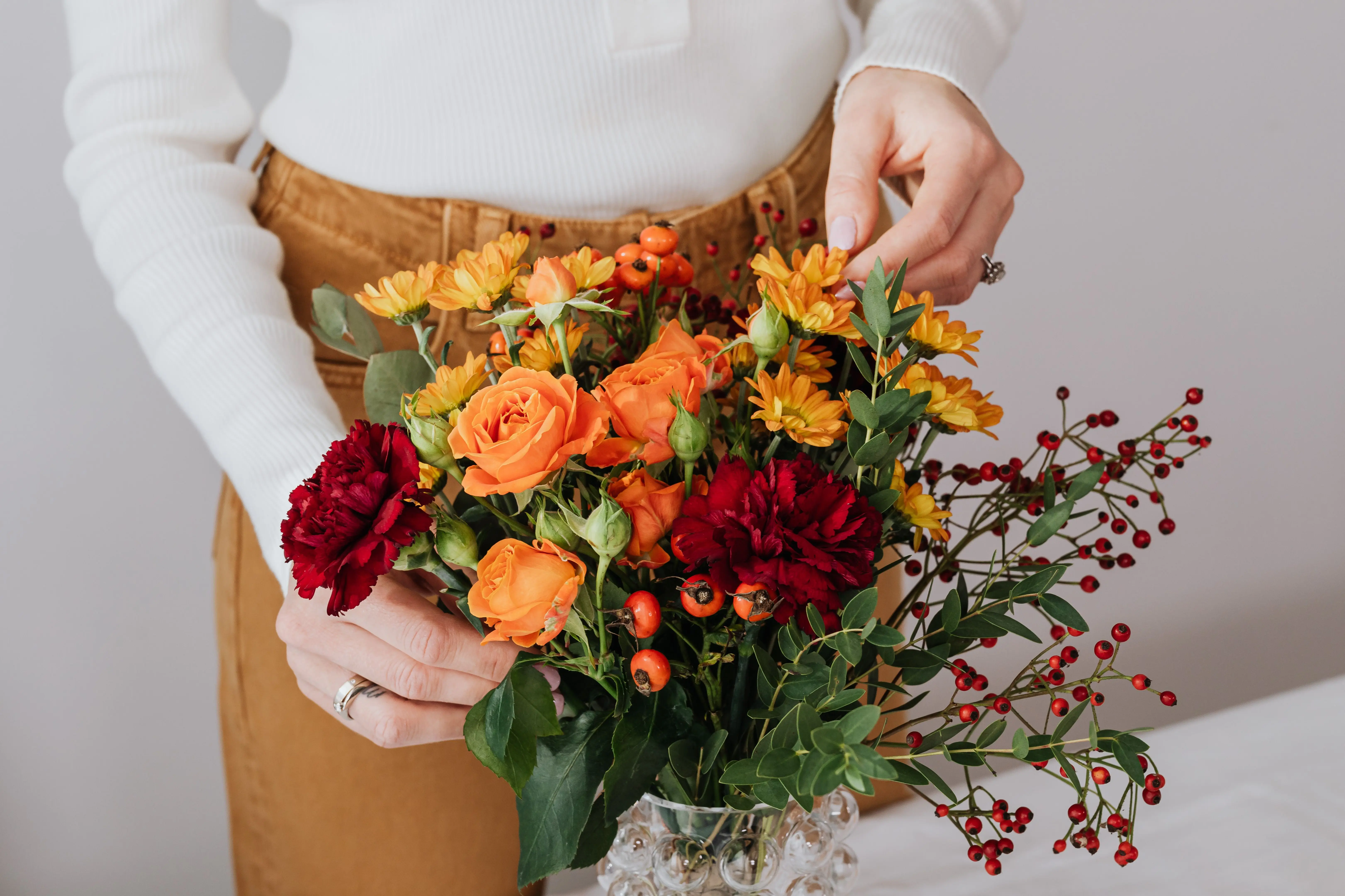 red flower plant A woman arranging a colorful floral bouquet with roses and chrysanthemums in a glass vase.