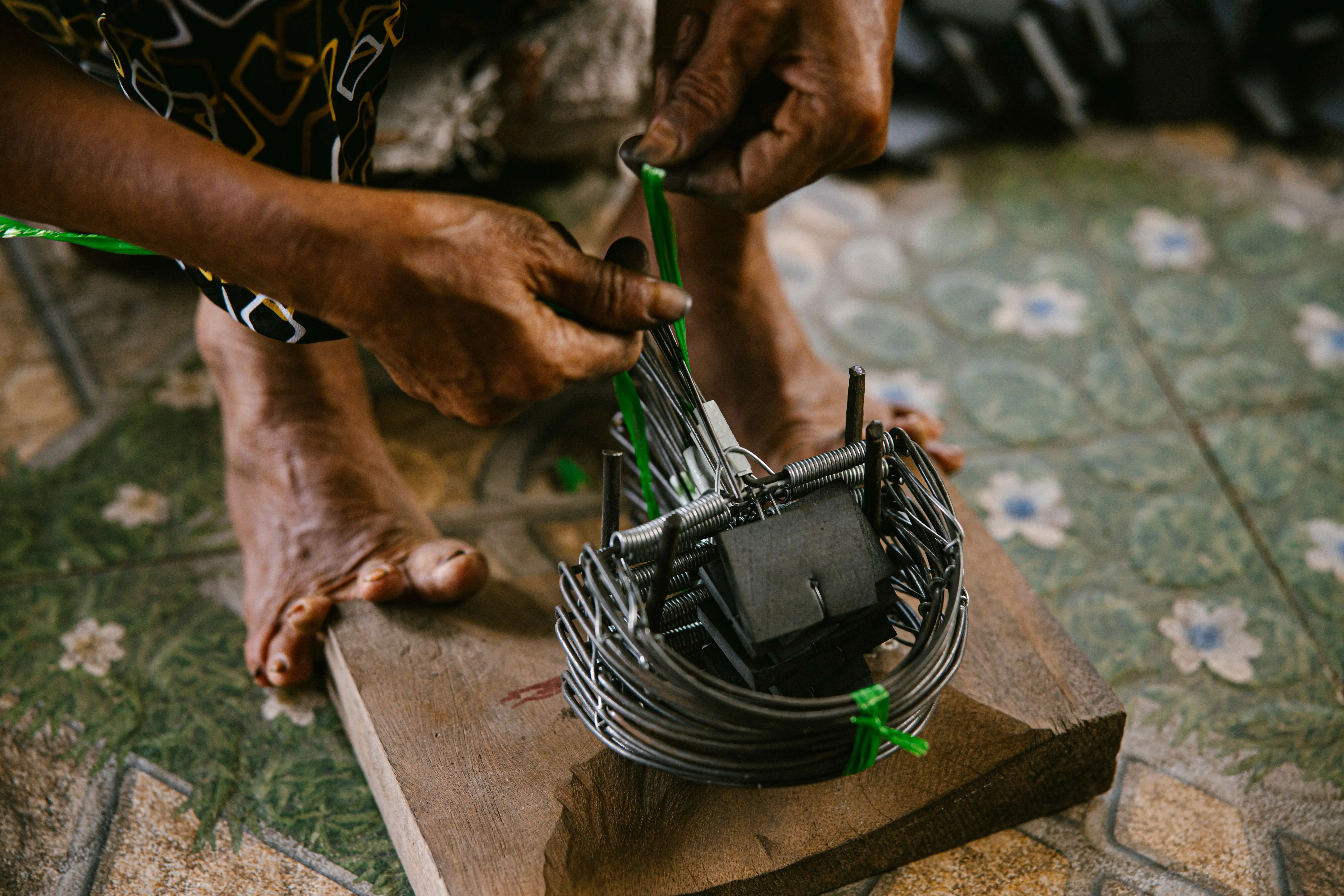 just one bite rat poison Craftsman's hands skillfully weaving a metal trap on wooden base indoors. Traditional craftsmanship.