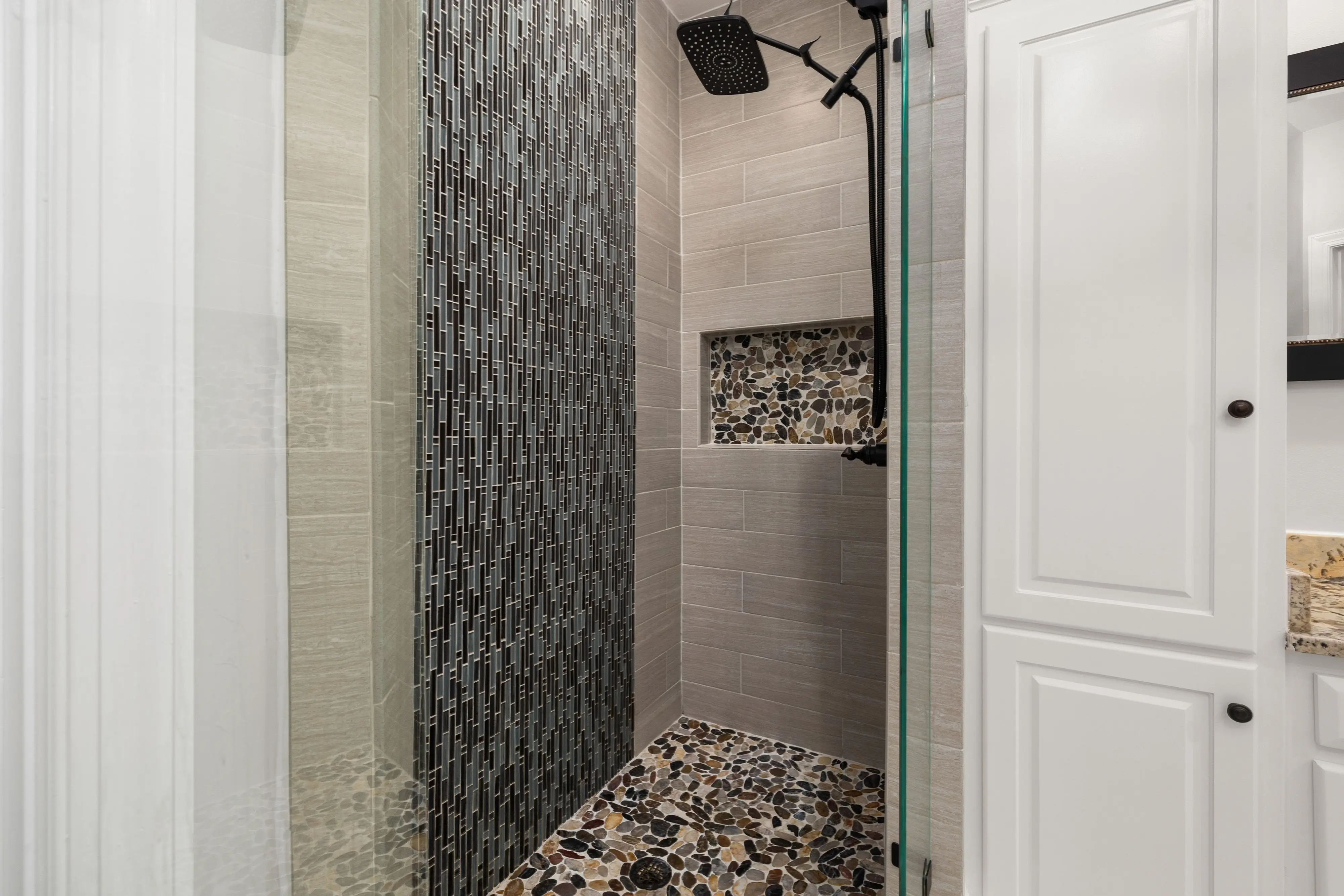 shower floors Contemporary shower featuring glass doors, mosaic tiles, and stone flooring in a modern bathroom.