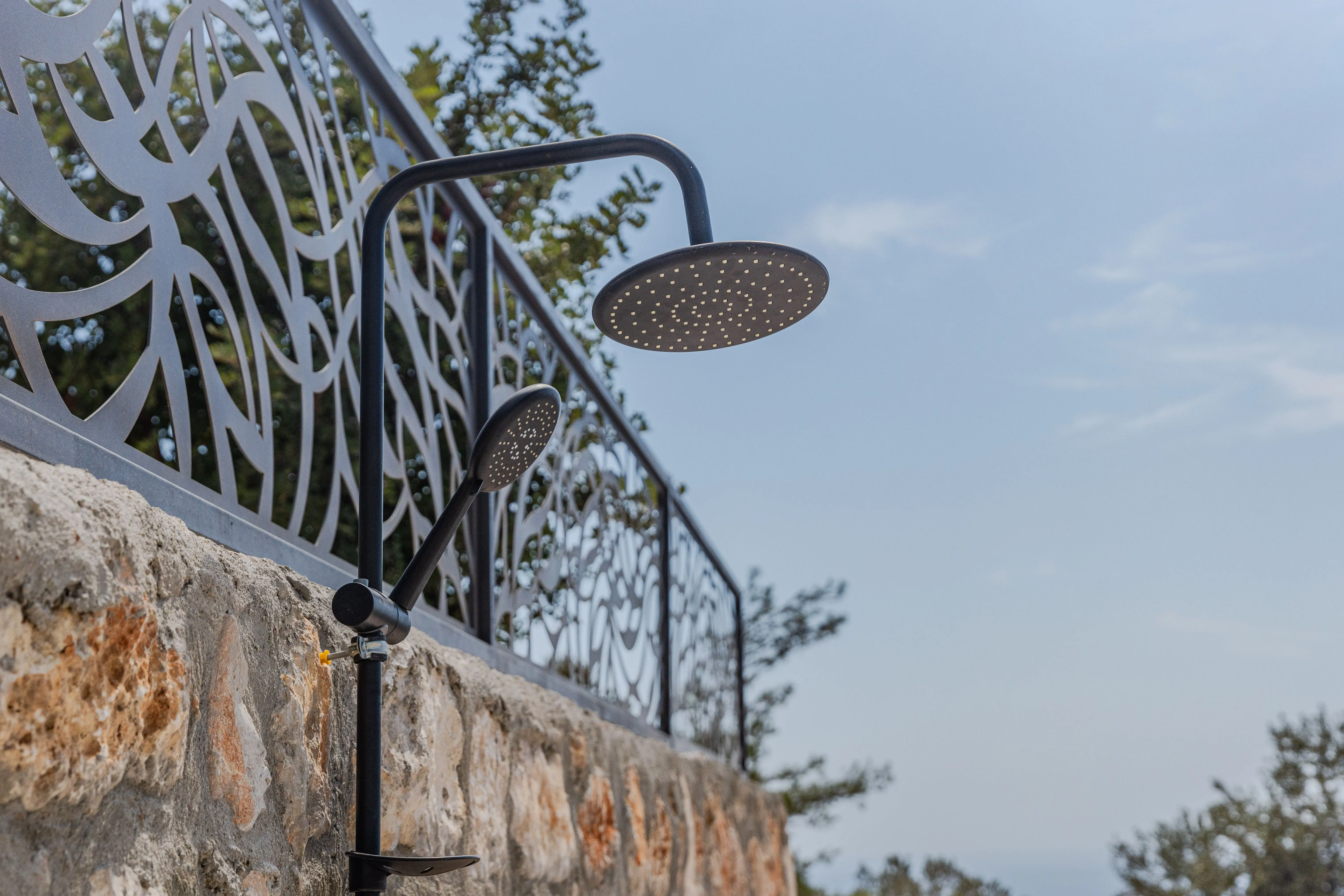 shower to bathtub conversion Outdoor shower setup with modern metal fence design against a stone wall under clear blue sky.