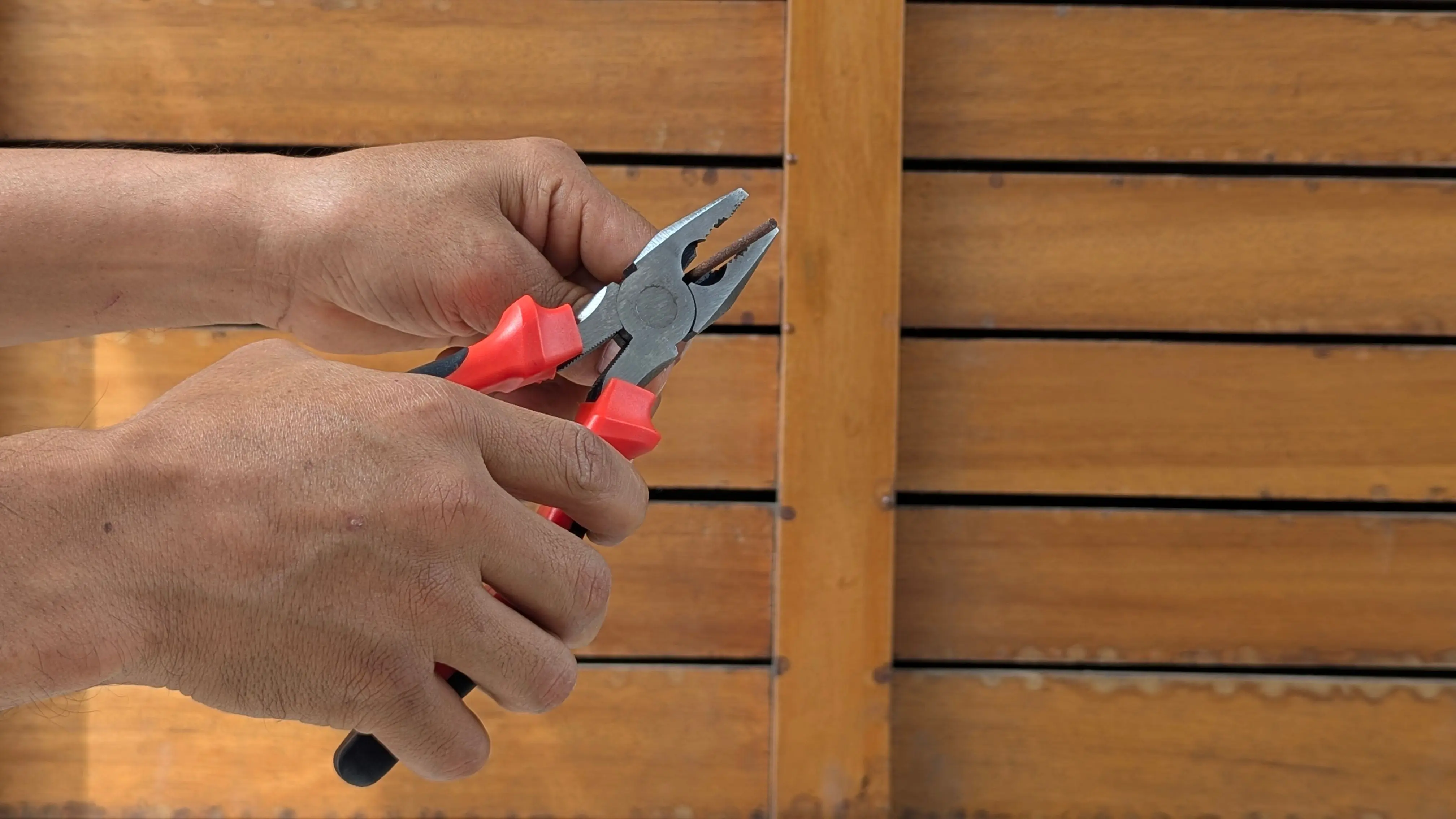 house siding ideas A detailed view of hands holding red pliers against a wooden backdrop, depicting a DIY or repair scene.