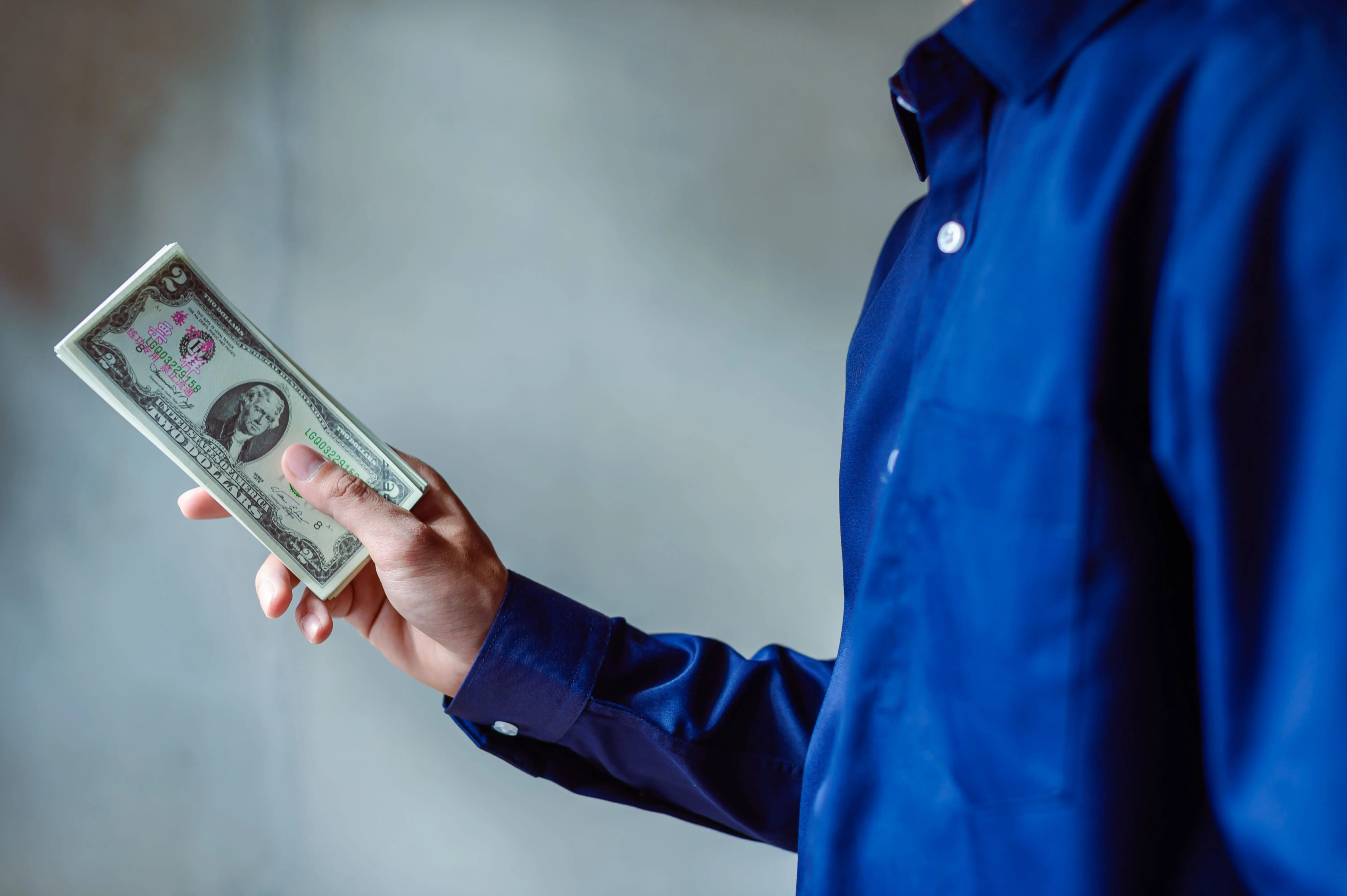 house siding ideas A person in a blue shirt holding a stack of US dollar bills, symbolizing wealth and finance.