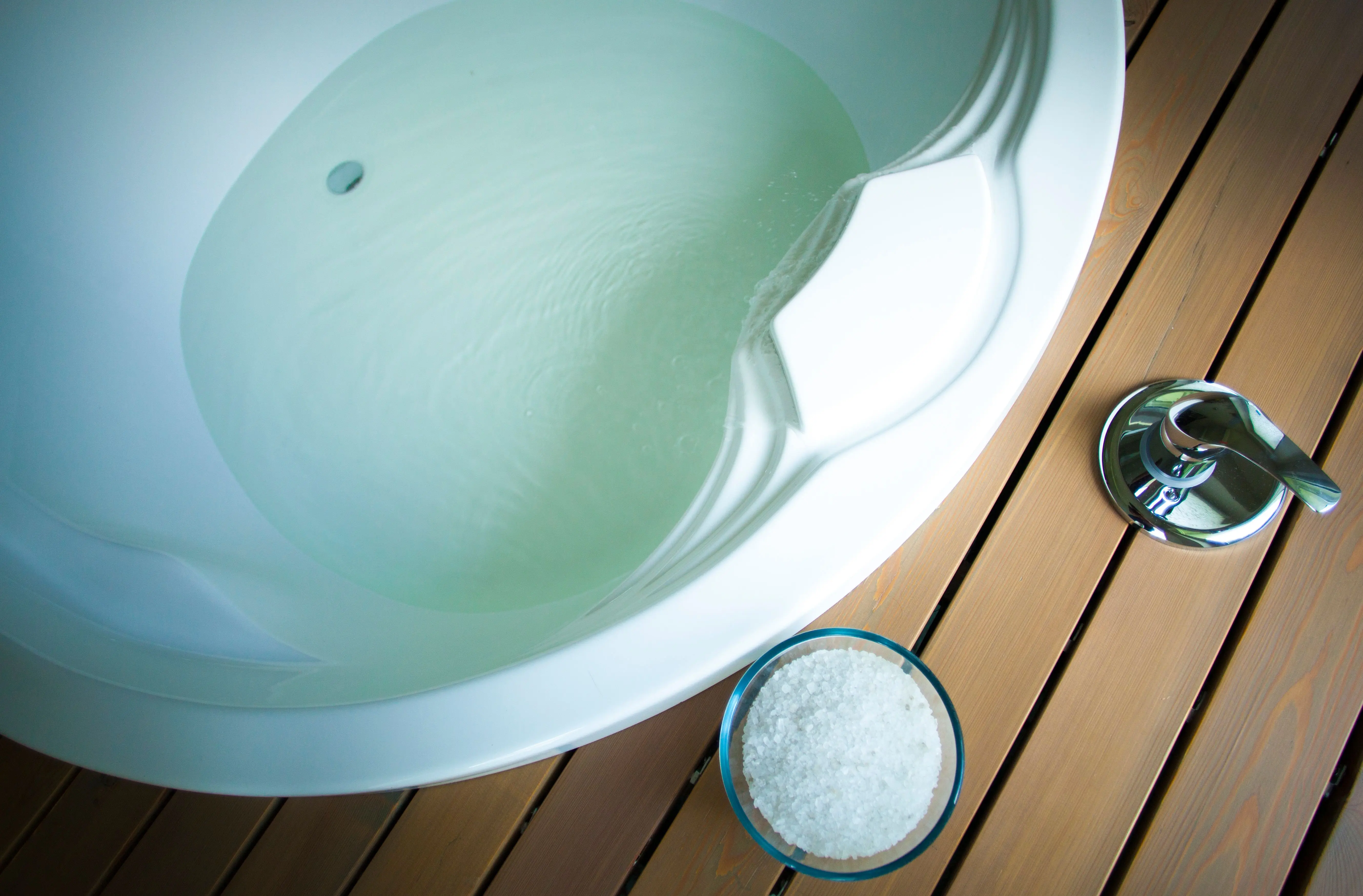 sink bath Top view of a white bathtub filled with water, complemented by a wooden deck and bath salts.