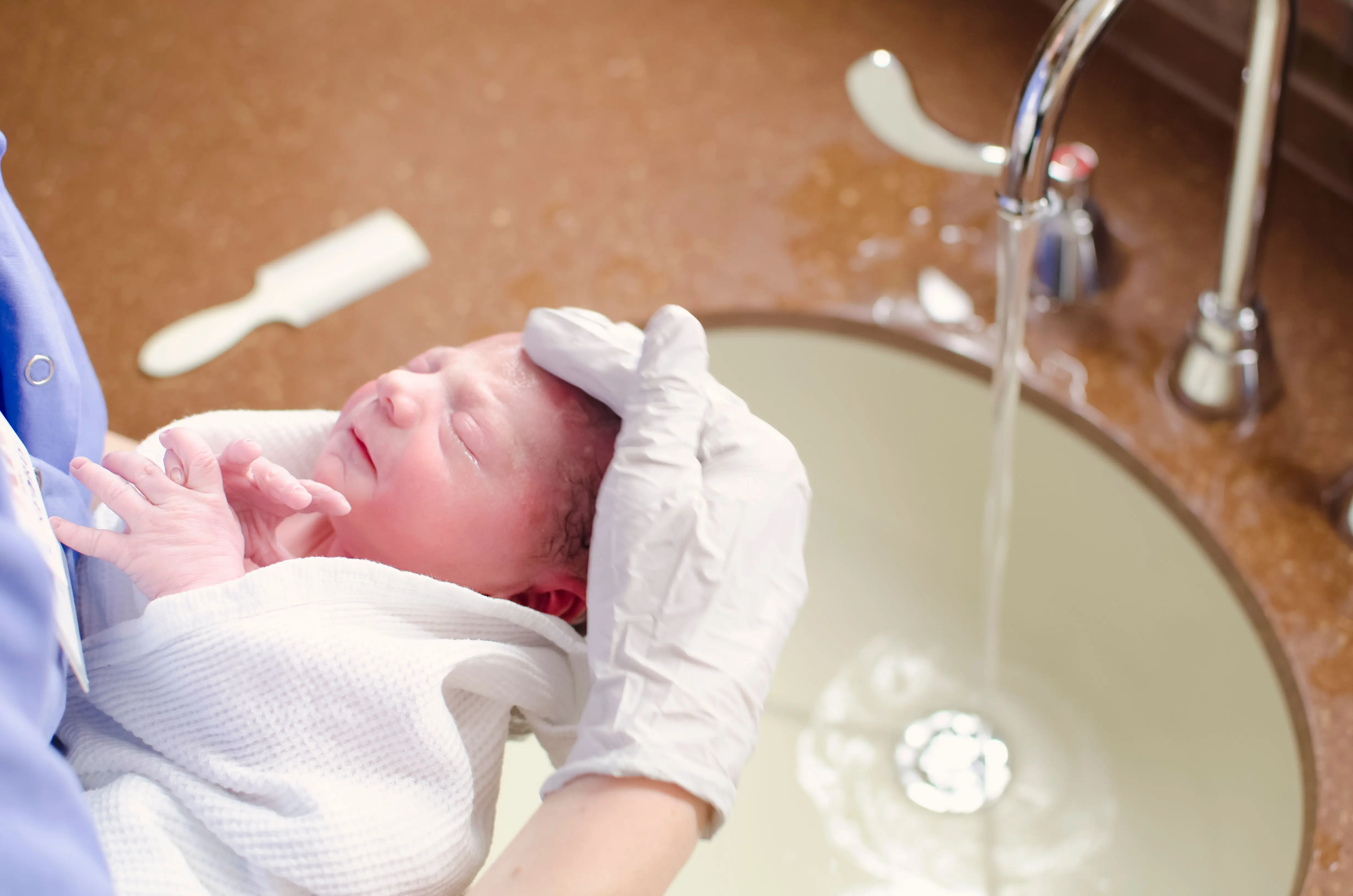 sink bath A nurse gently bathes a newborn in a hospital sink, ensuring care and hygiene.