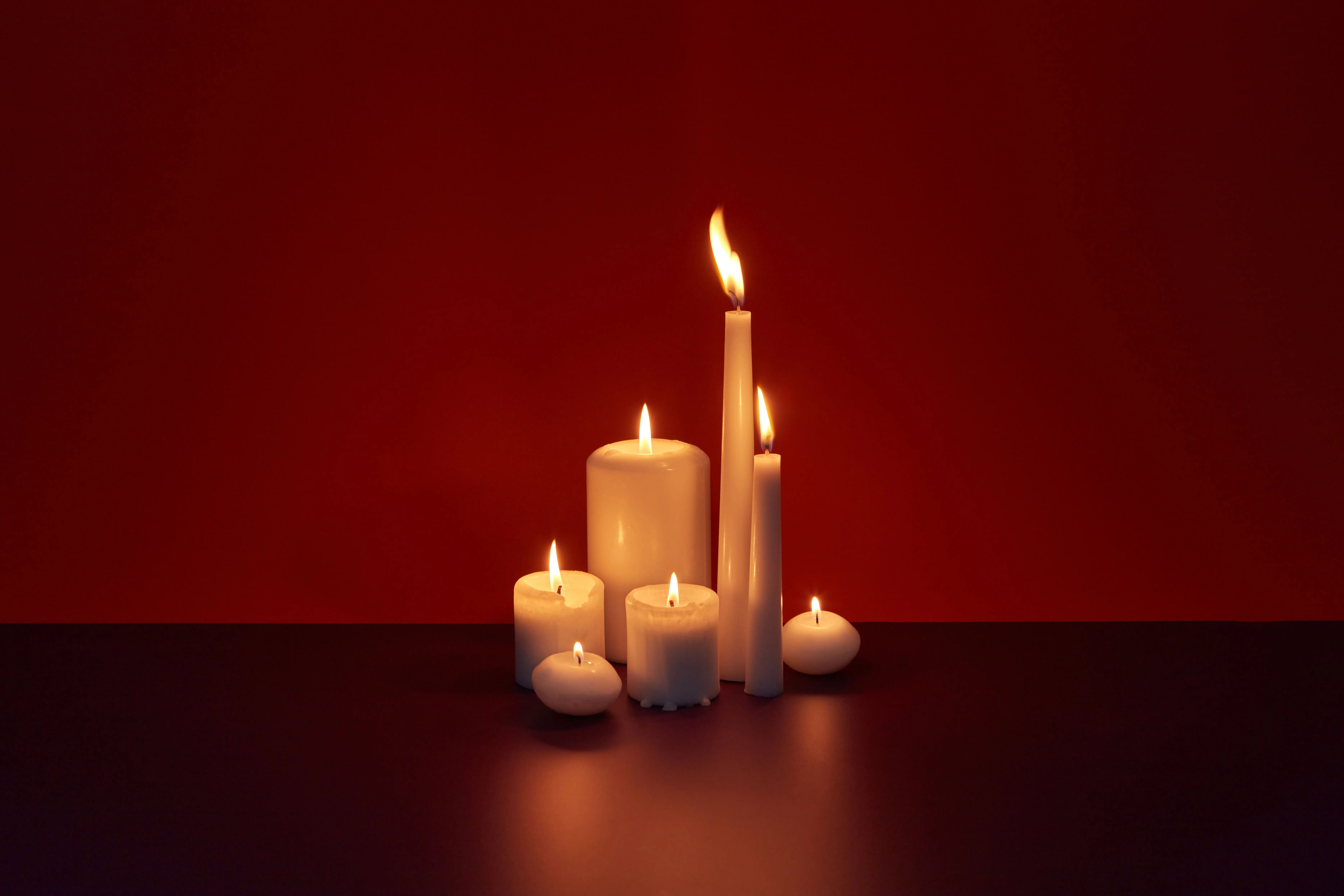 tapered candle holders A tranquil display of glowing white candles against a rich red background creating a serene ambiance.