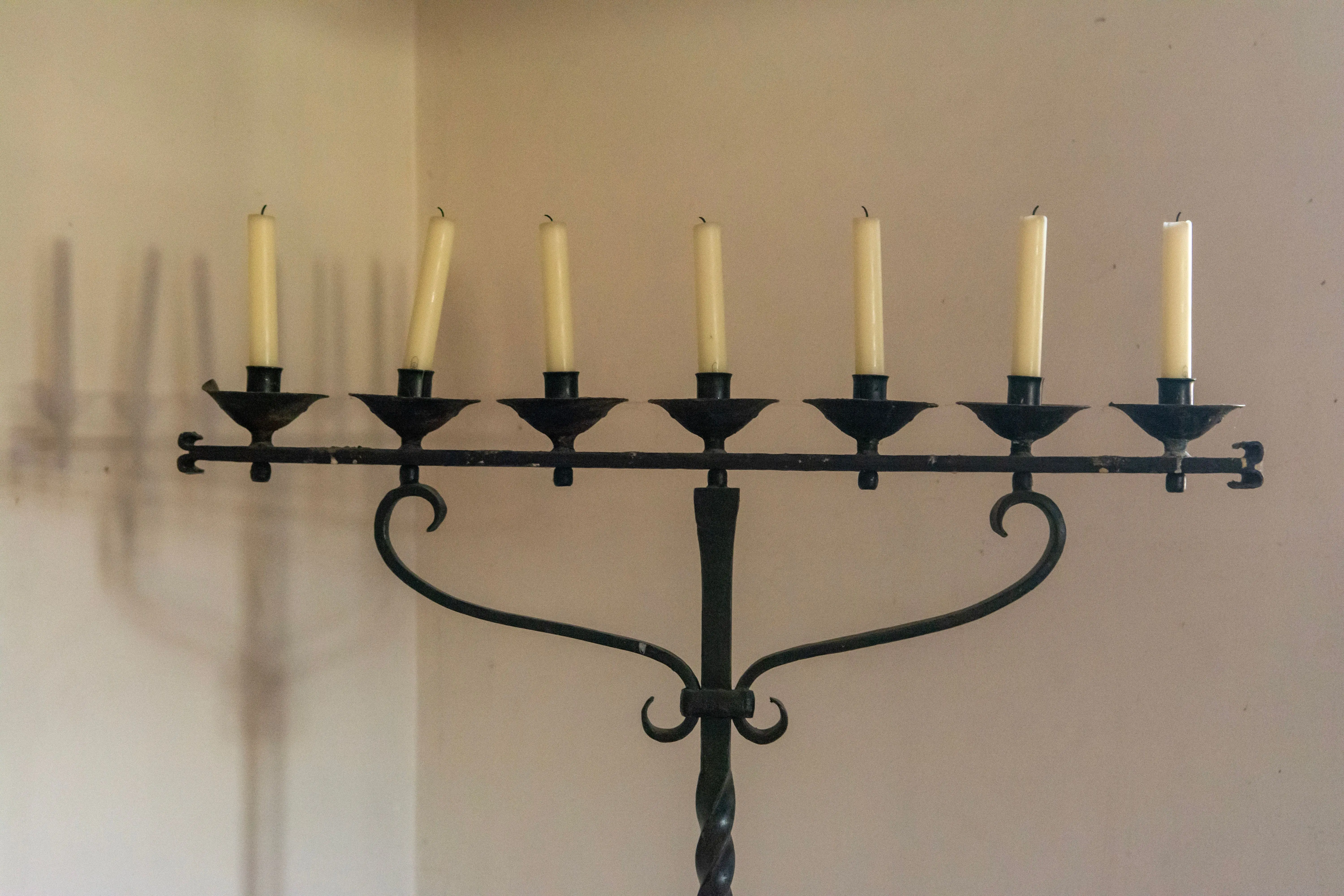 tapered candle holders Close-up of an antique metal candle holder with lit candles, casting intricate shadows on the wall.