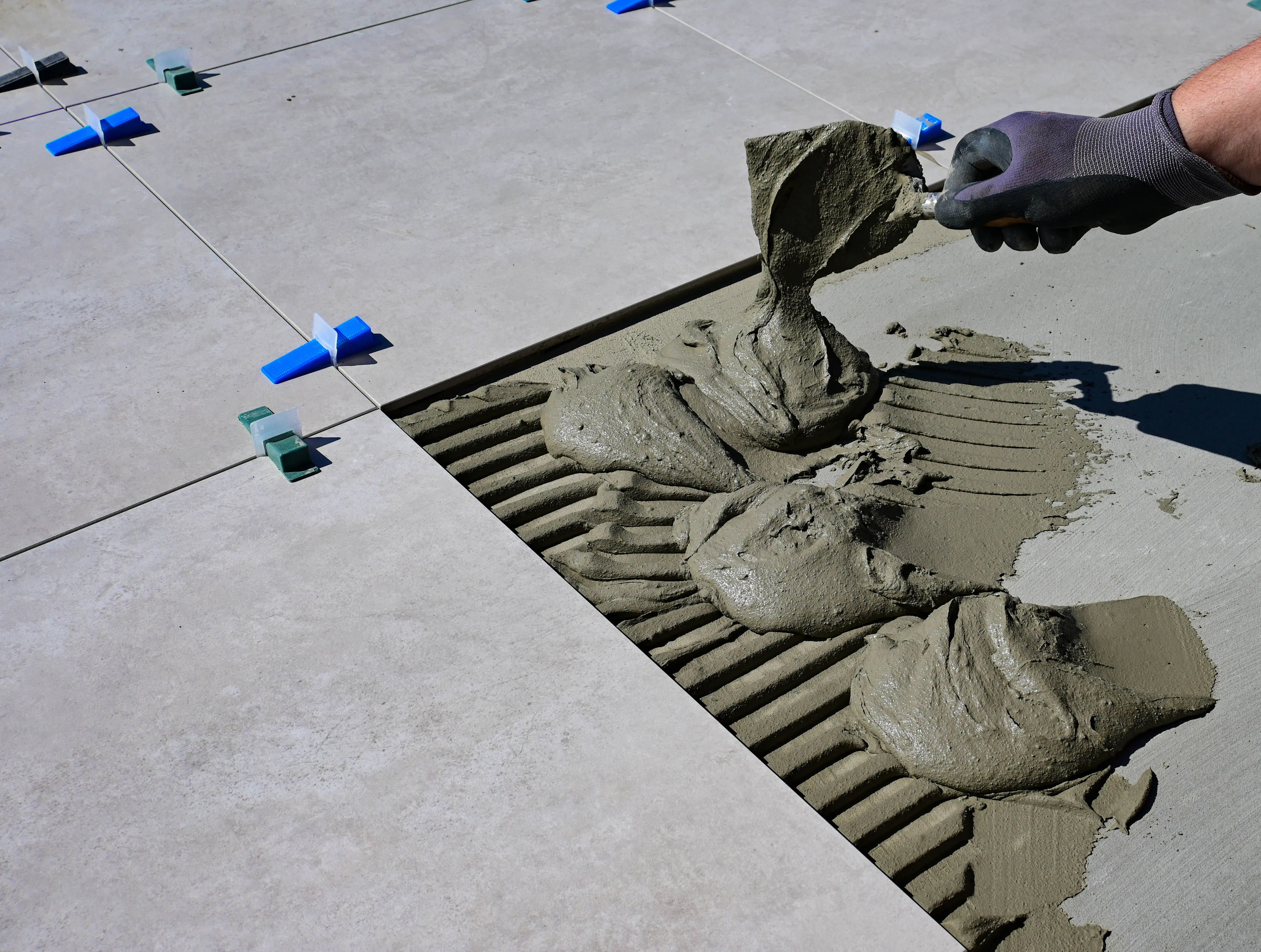 tiling glass tiles Close-up of a gloved hand applying mortar for ceramic tile installation outdoors.