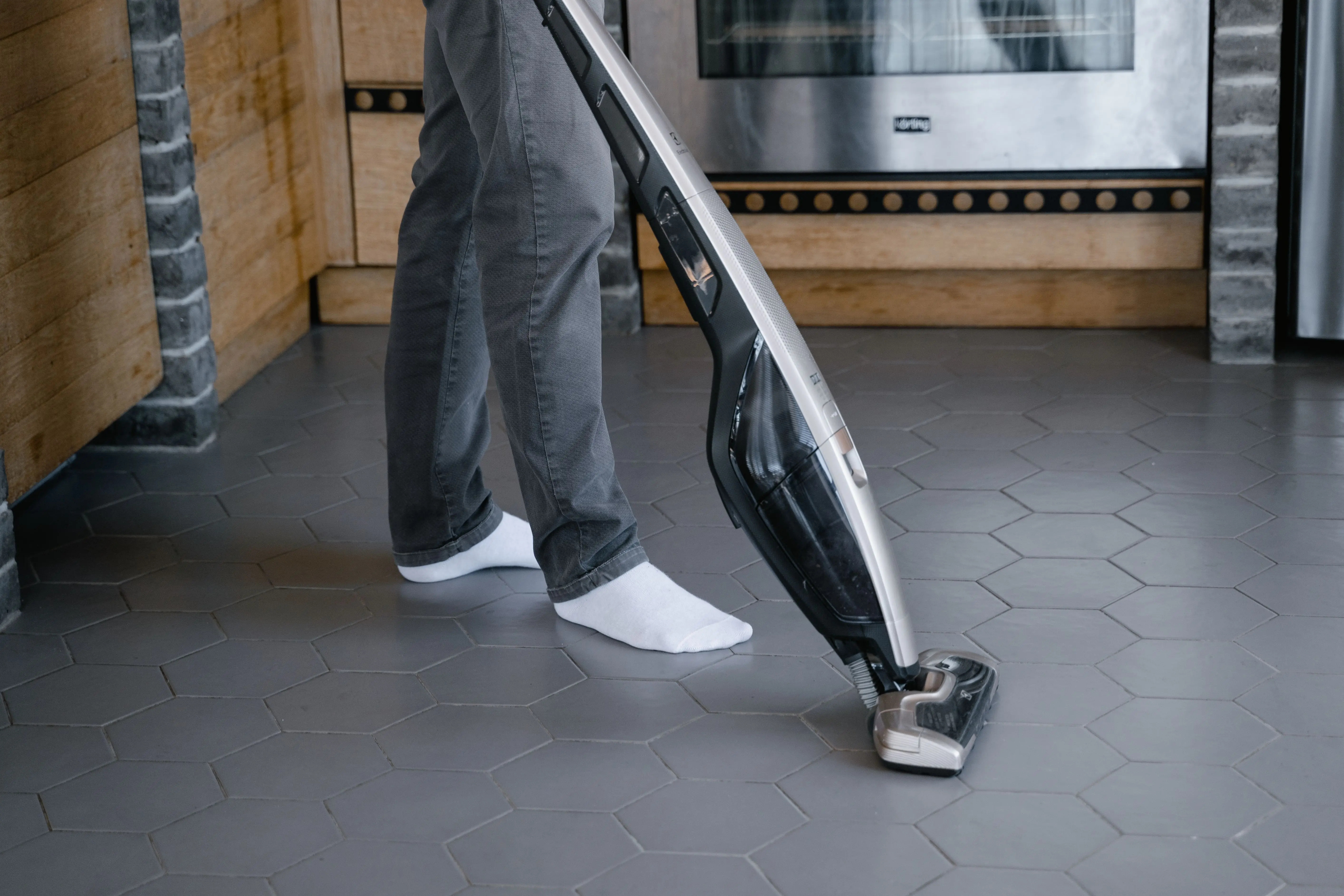 vacuum hoovers A person cleaning a tiled floor with a modern vacuum cleaner indoors.