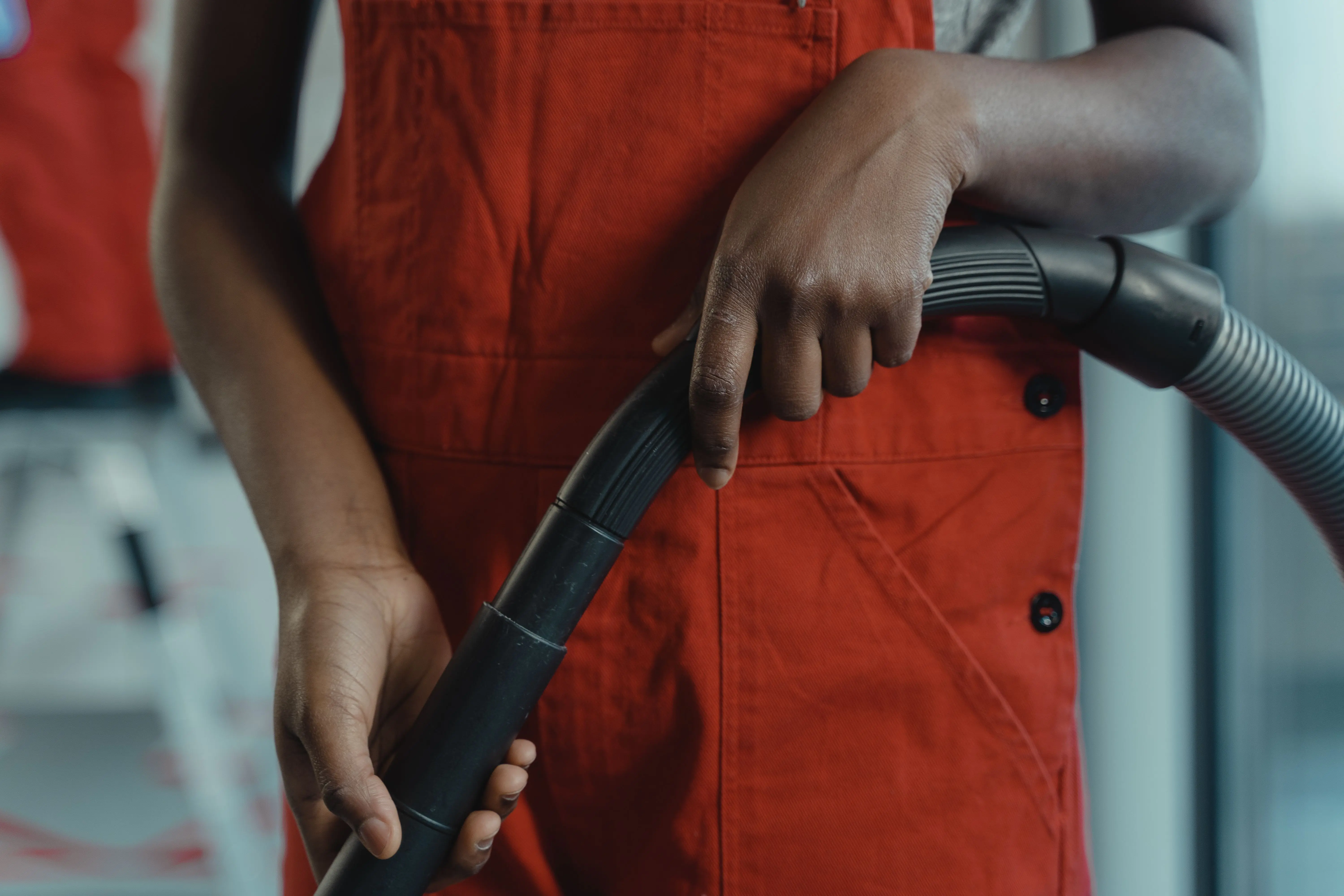 vacuum hoovers A person in a red apron holding a vacuum cleaner hose during indoor cleaning.