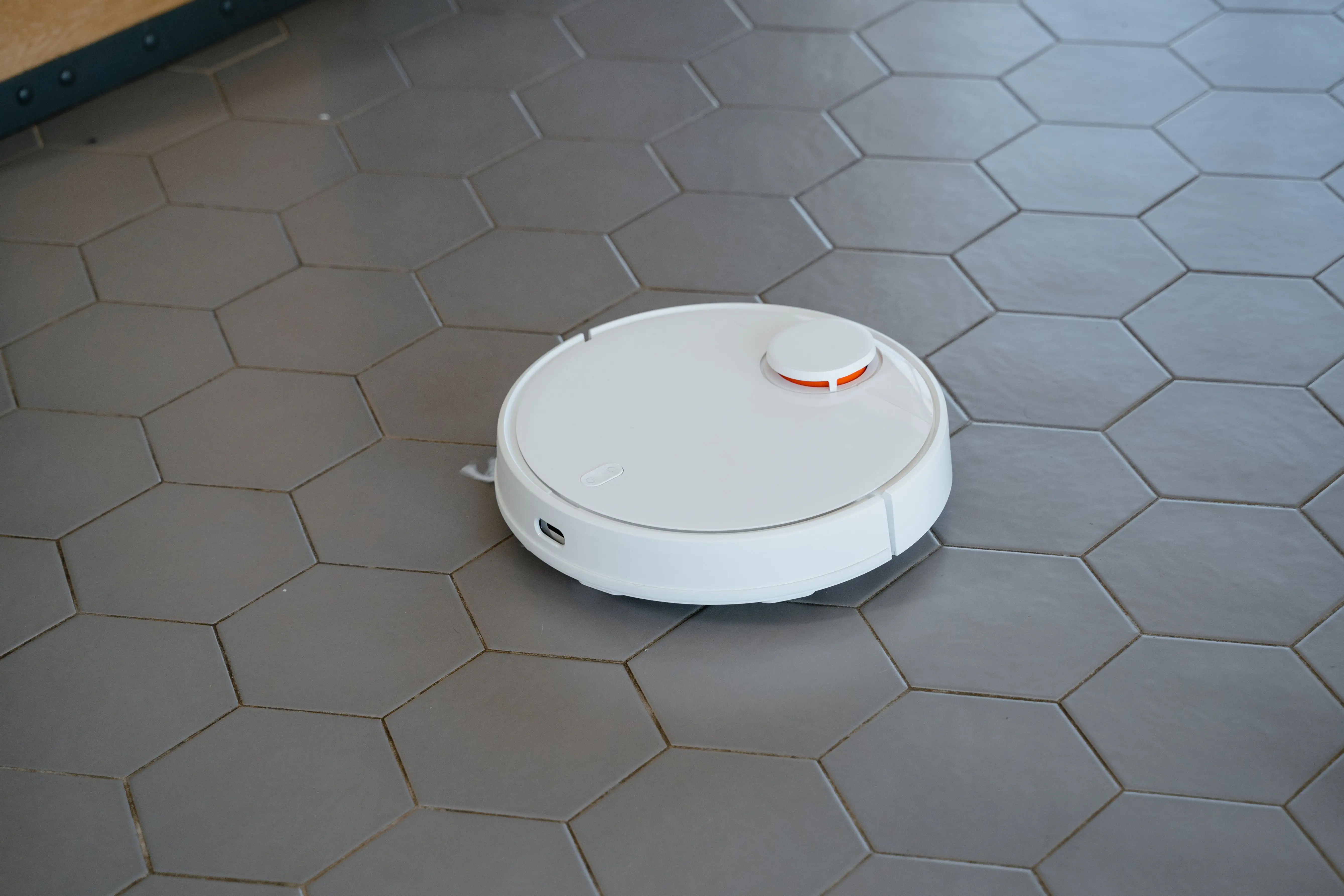 vacuum hoovers A sleek, white robotic vacuum cleaner operating on a hexagonal tiled floor.