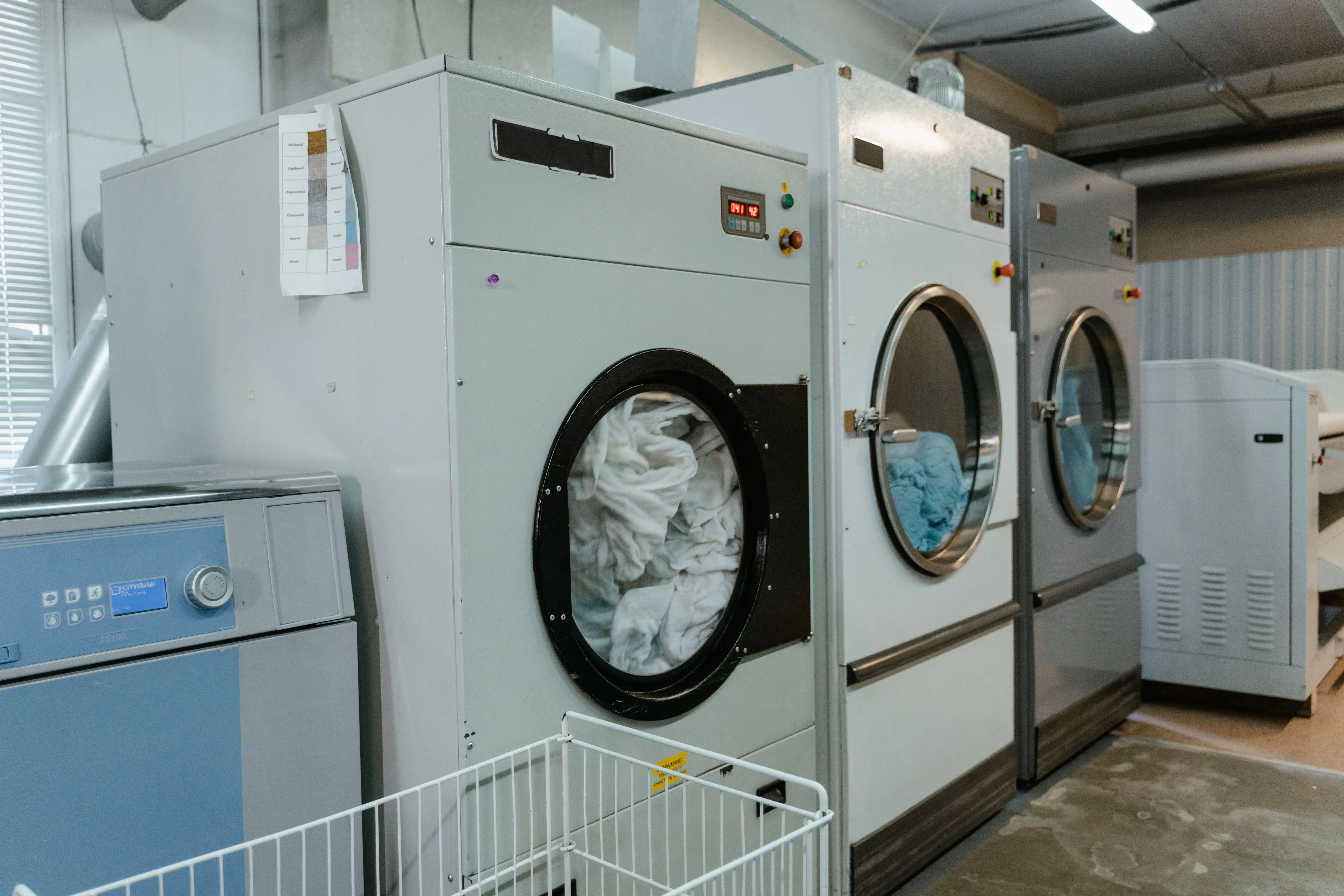 washer sizes Interior view of industrial laundry machines in a facility with linens being washed.