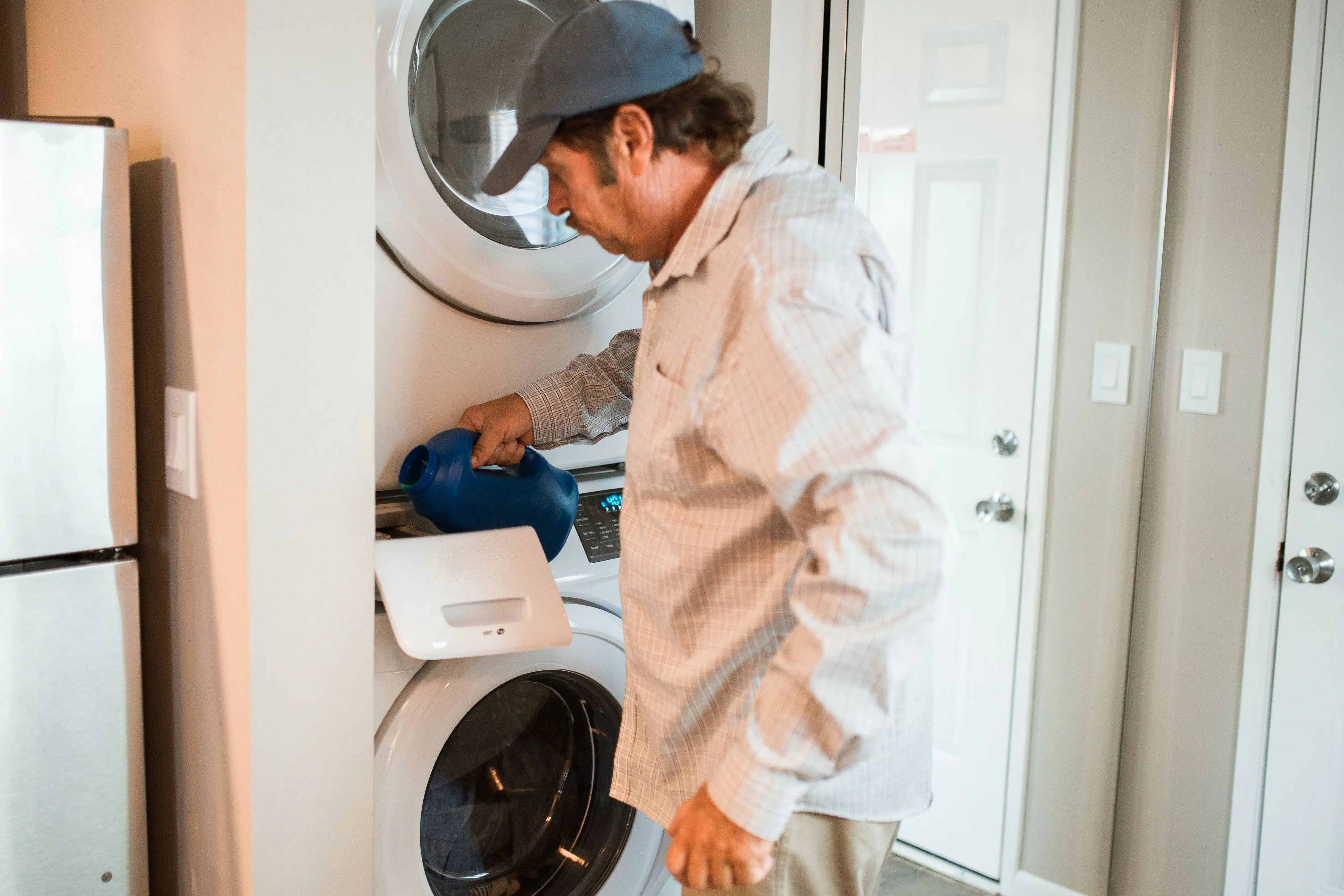 how much does a washer weigh Man pouring liquid detergent into a stacked washer and dryer in a modern laundry room.