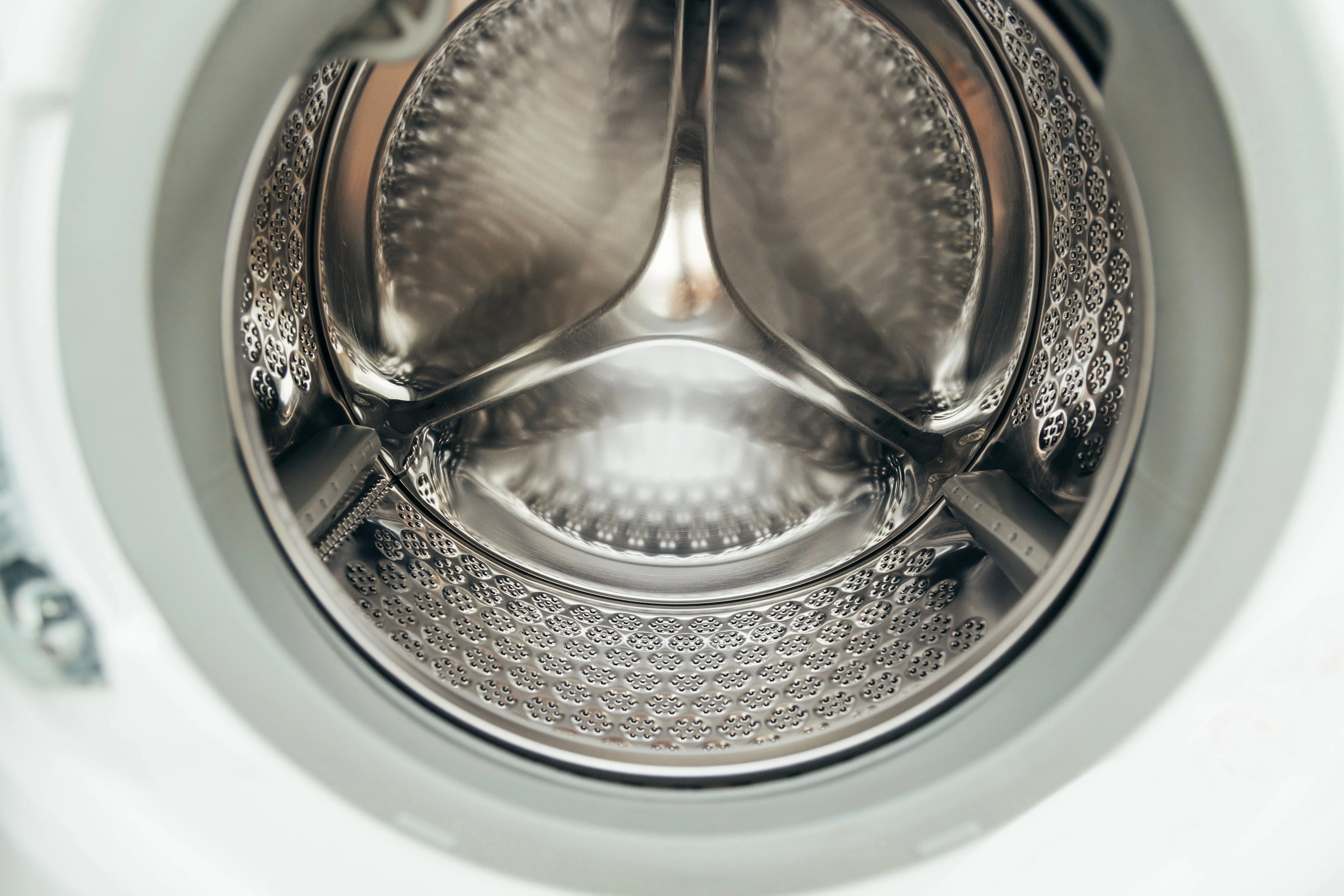 washer sizes Detailed view of a clean, modern washing machine drum, showcasing shiny stainless steel interior.