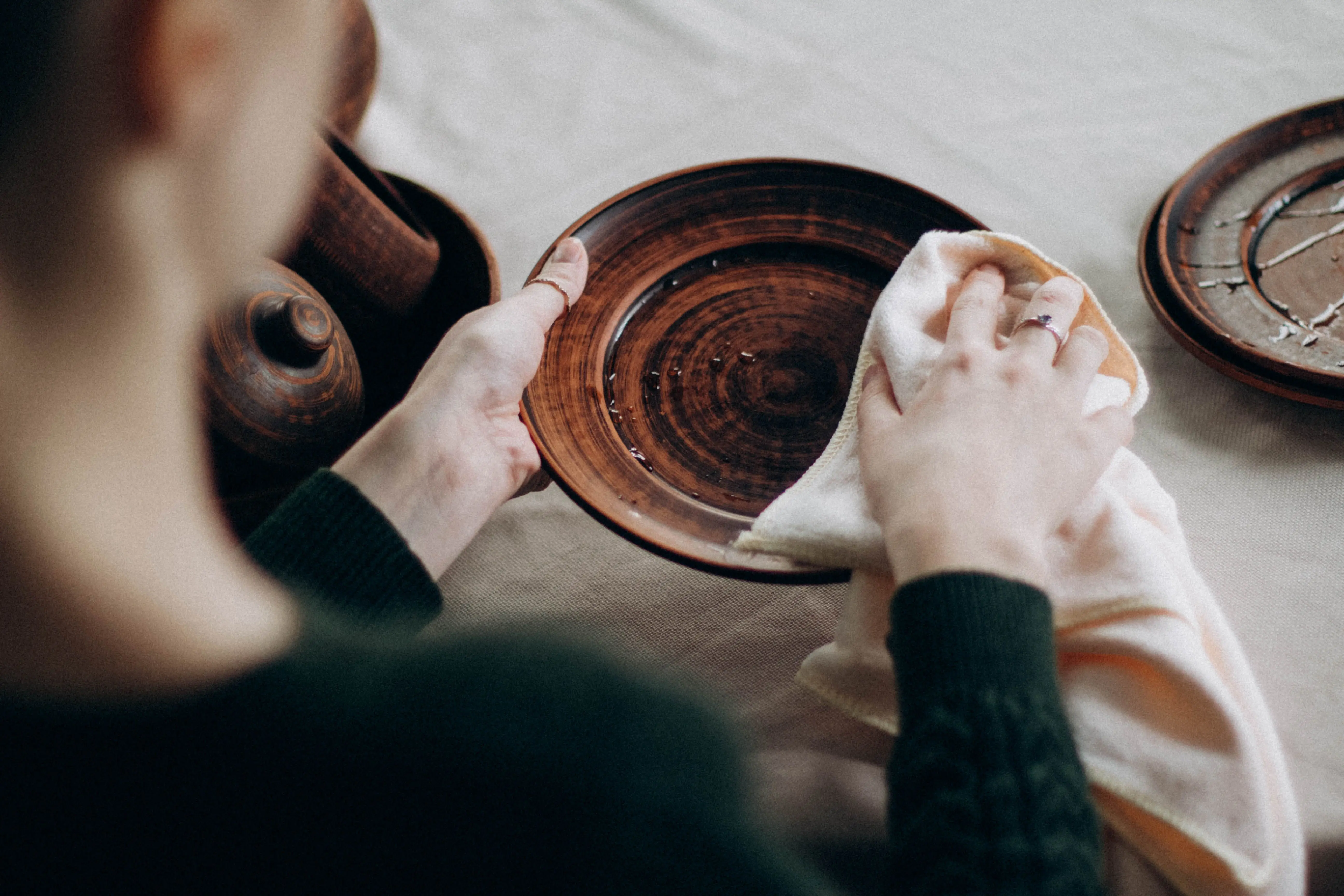 kitchen work table A woman cleaning a wooden plate on a table with a towel in a cozy setting.