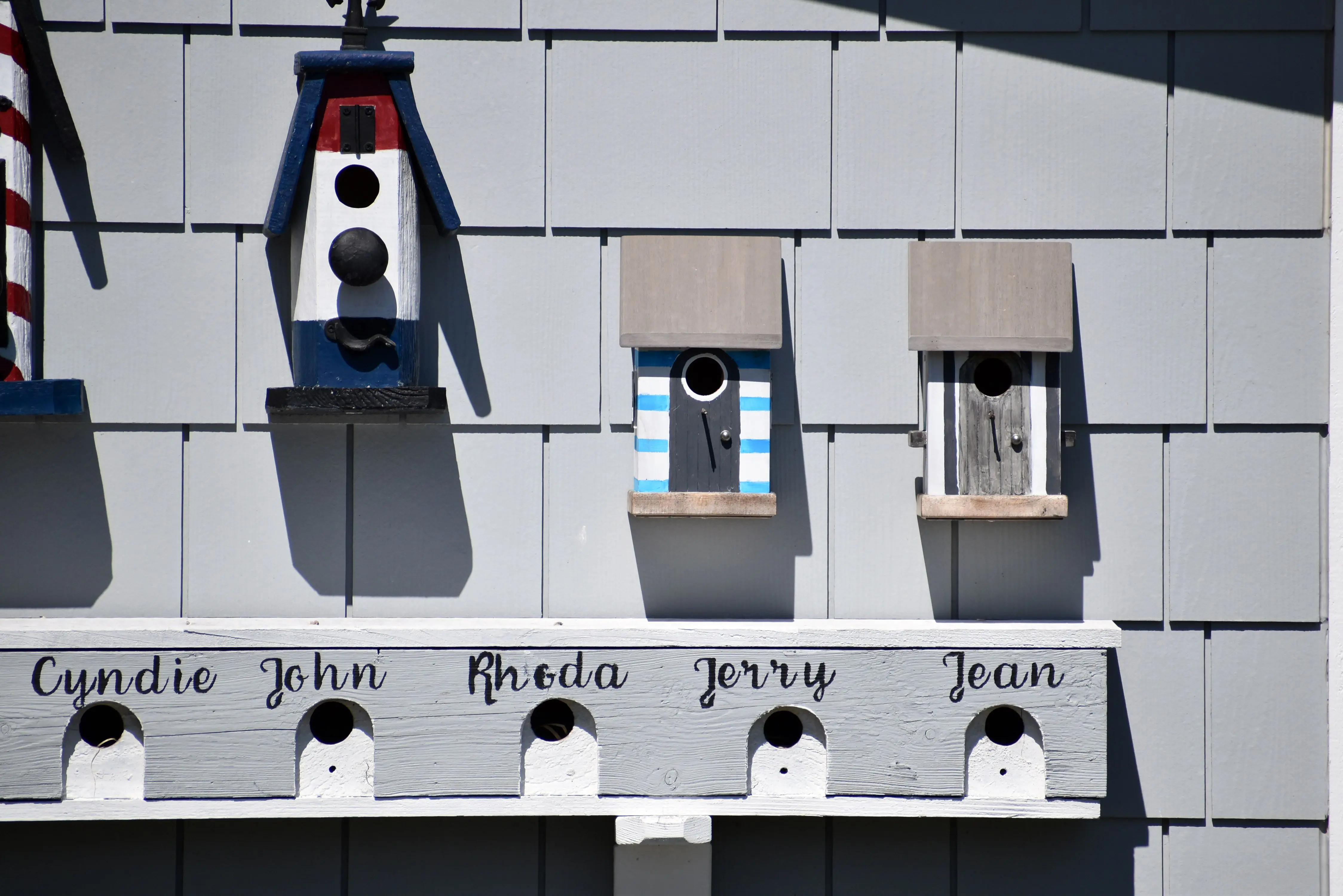 birdhouse kit Charming birdhouses with names displayed on an exterior wall under bright sunlight.