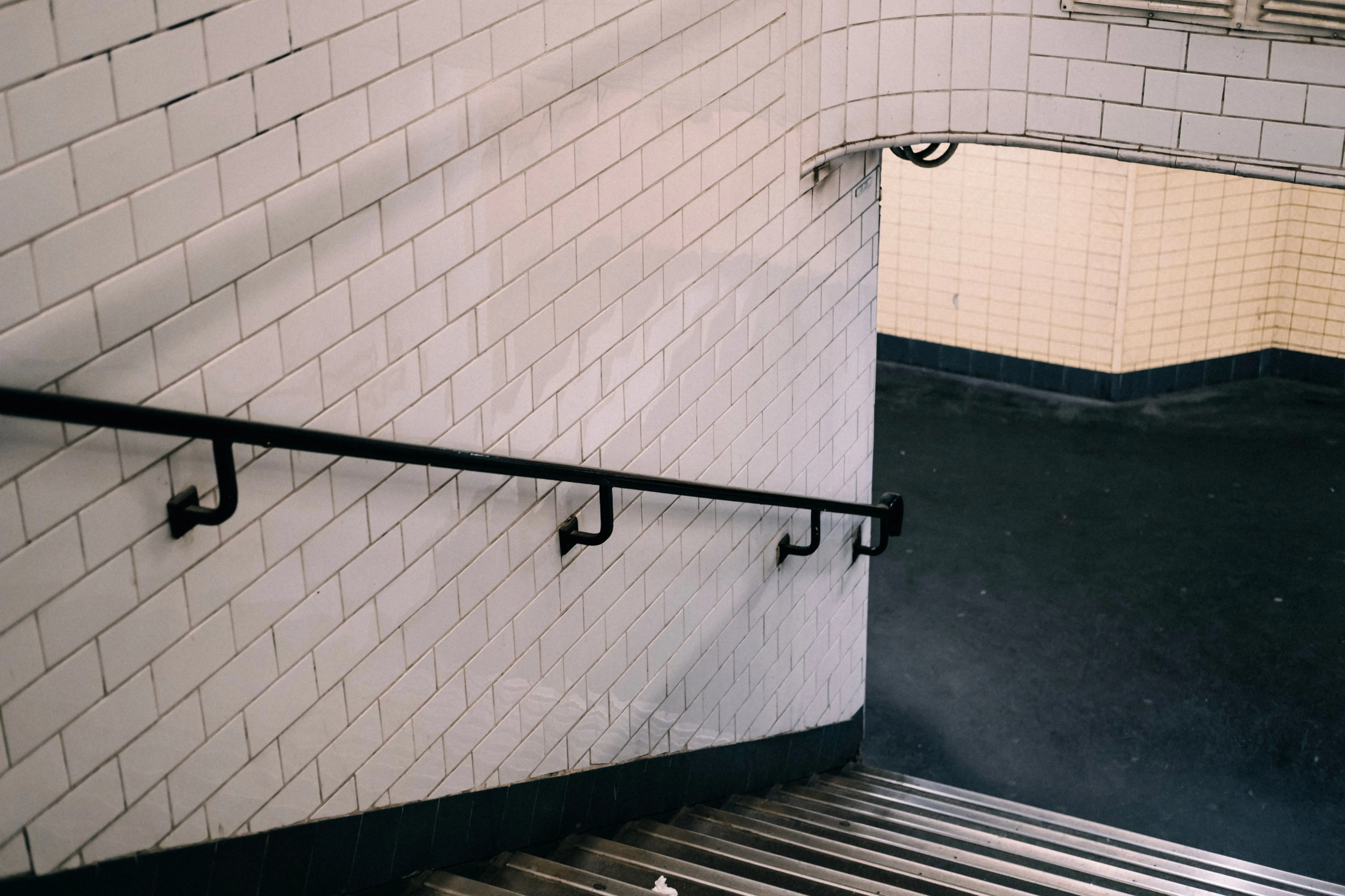black subway tile A staircase in an underpass with white tiled walls and a metal railing, creating an urban feel.